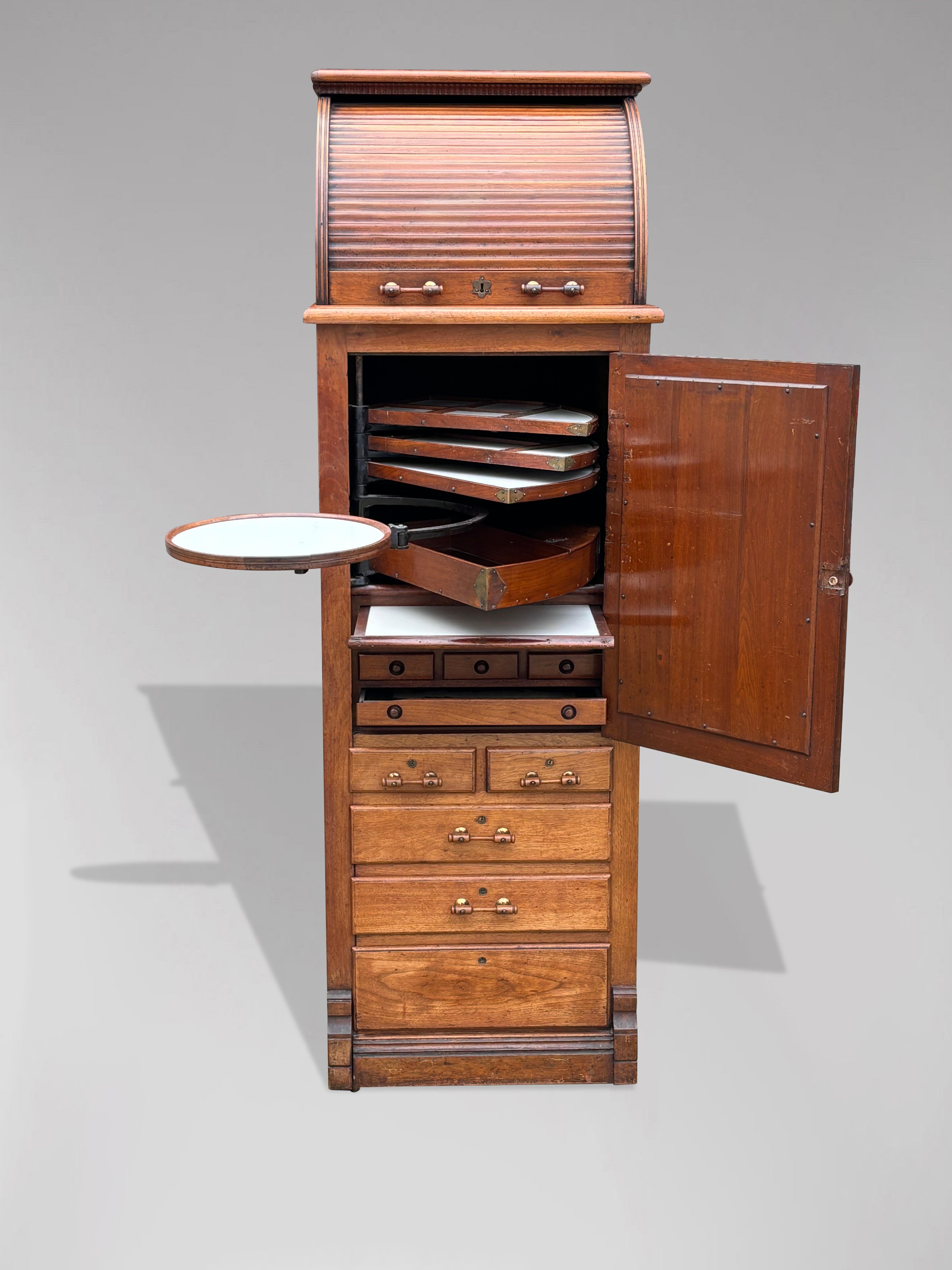 A 19th century oak dental cabinet, made by the Harvard & Co. in Canton, Ohio. This is the deluxe model made of quarter sawn oak with a finished back. An oak tambour roll over top section, above a cabinet with original bevelled glass mirrored door,
