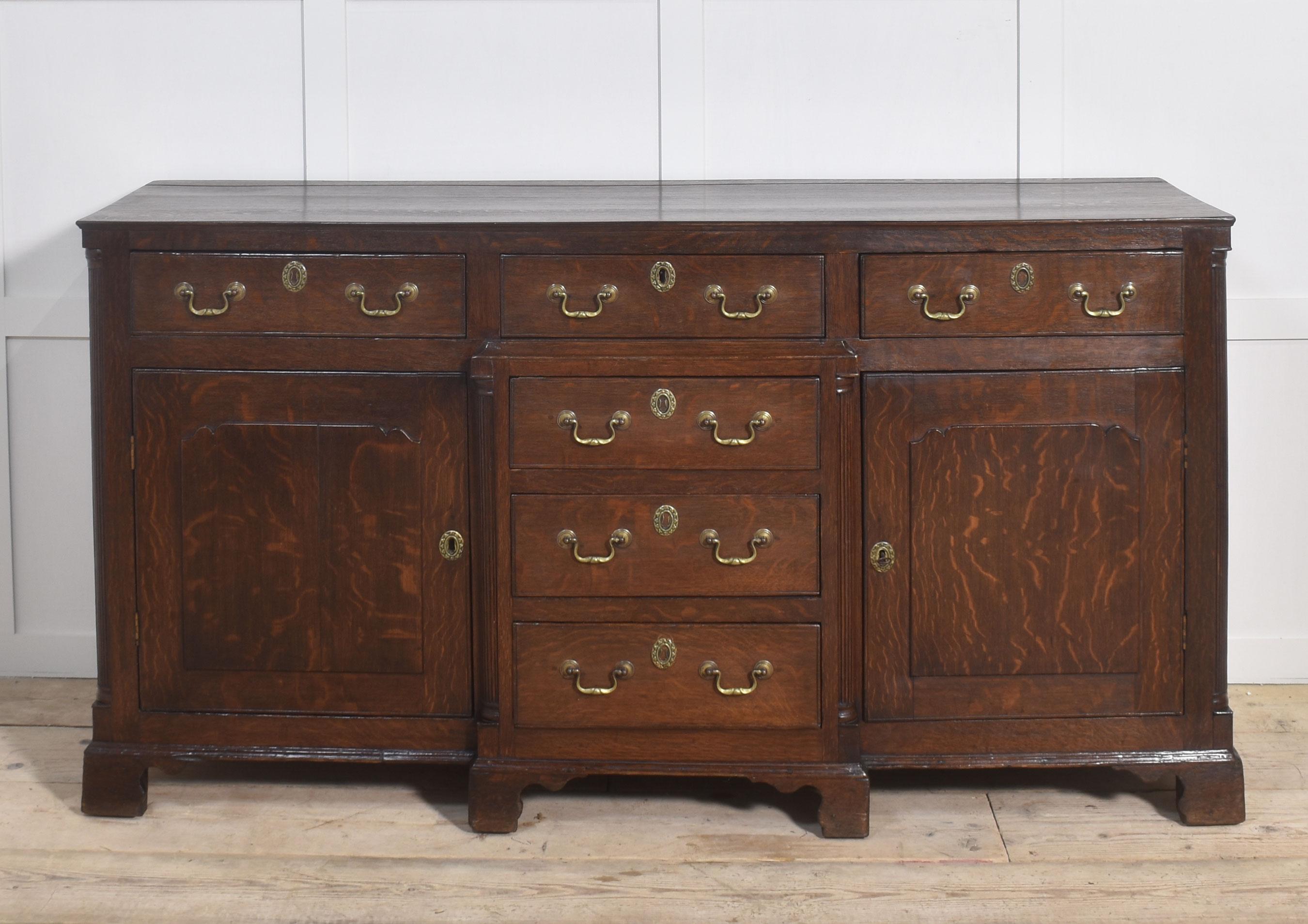 Base per comò in Oak, con piano d'appoggio su tre cassetti a fregio con maniglie a collo di cigno in ottone e circolare sopra altri tre cassetti fiancheggiati da ante di armadietti pannellati che si aprono per rivelare l'interno a ripiani. Il tutto