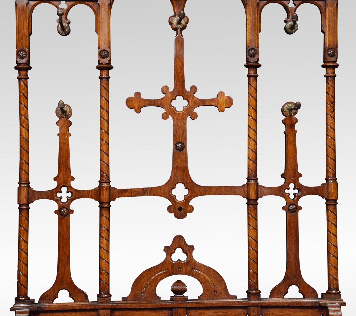19th century oak hall stand in the manner of Pugin. The chamfered top above ornately carved superstructure fitted with five coat hooks with acorn finials. The base having an umbrella stand with a tin lined removable drip tray all raised up on plinth