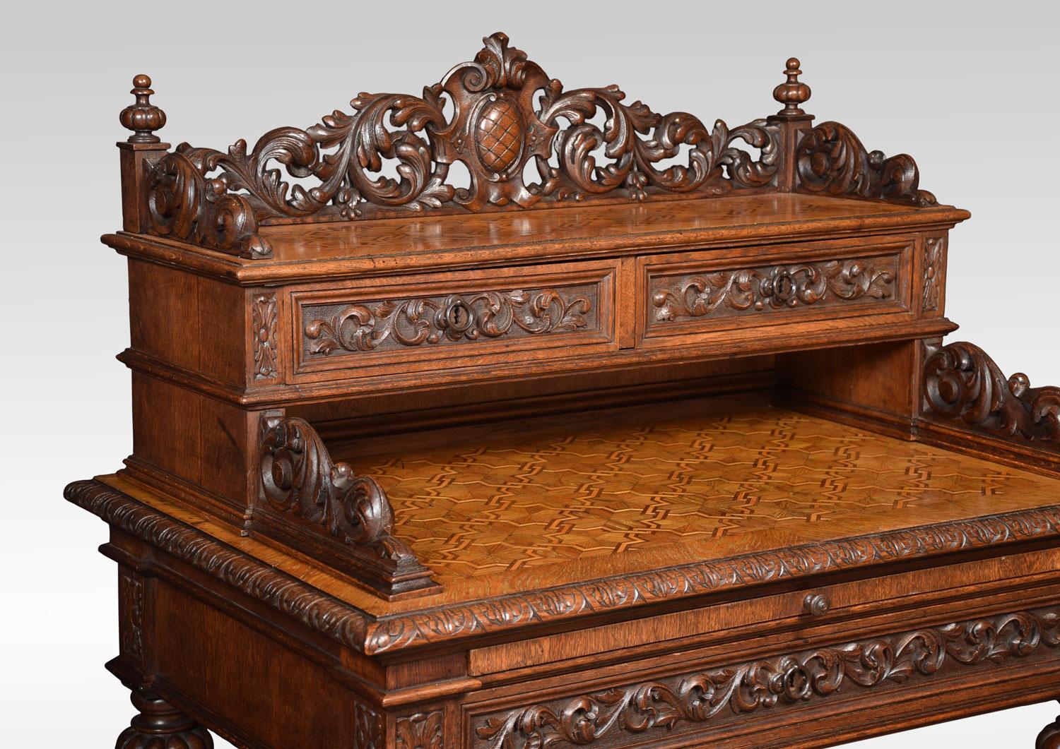 French oak writing desk, having foliate carved three quarter gallery above two short drawers. The moulded rectangular parquetry top fitted with pull out inset black leather writing slide and large frieze draw below. All raised up on fluted baluster