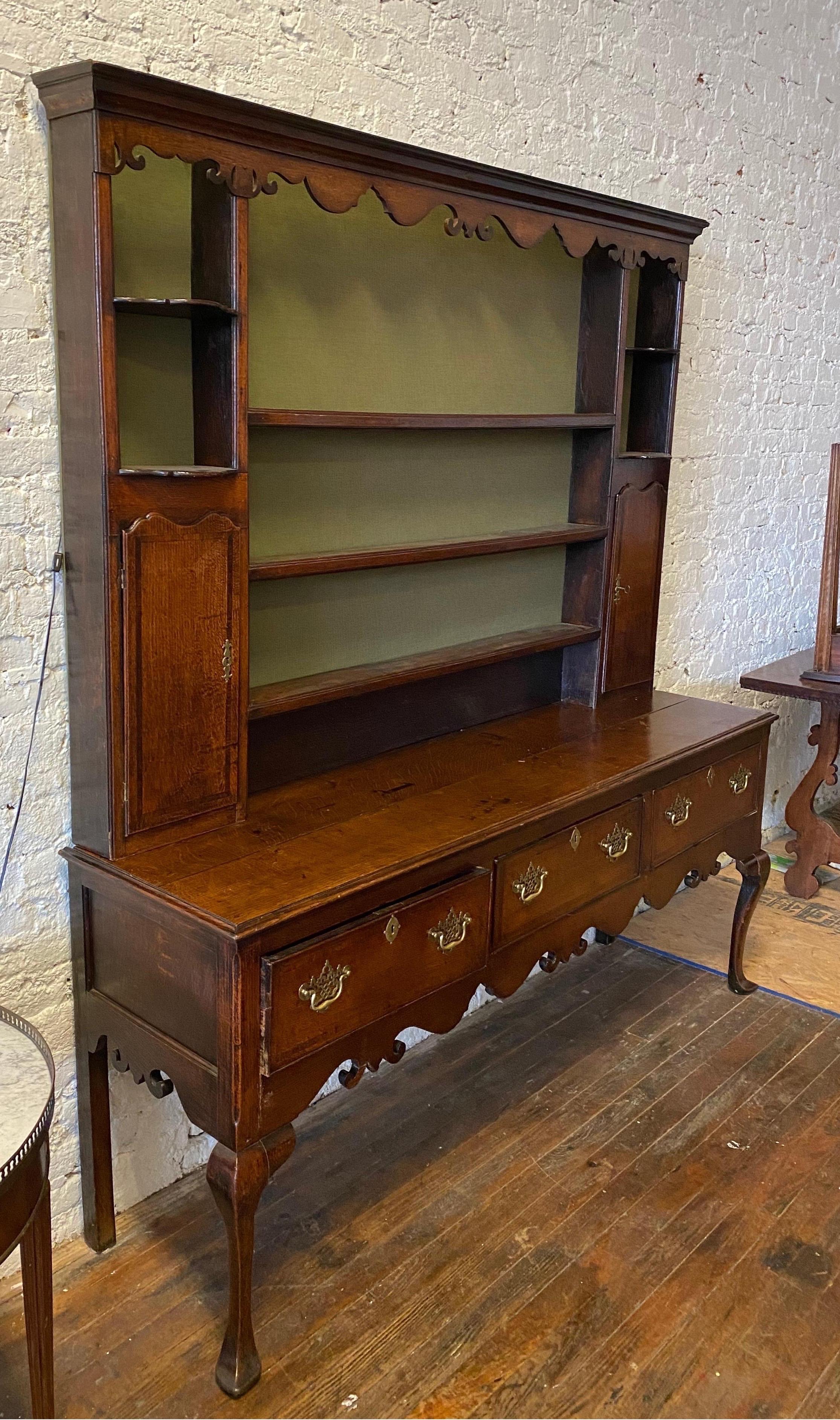 19th century oak welsh cupboard with 3 drawers over a carved apron and cabriole legs. The top rack separates and has matching carvings, two spice cabinets, shelves and has had a very nice green backing and lights added in the crown.