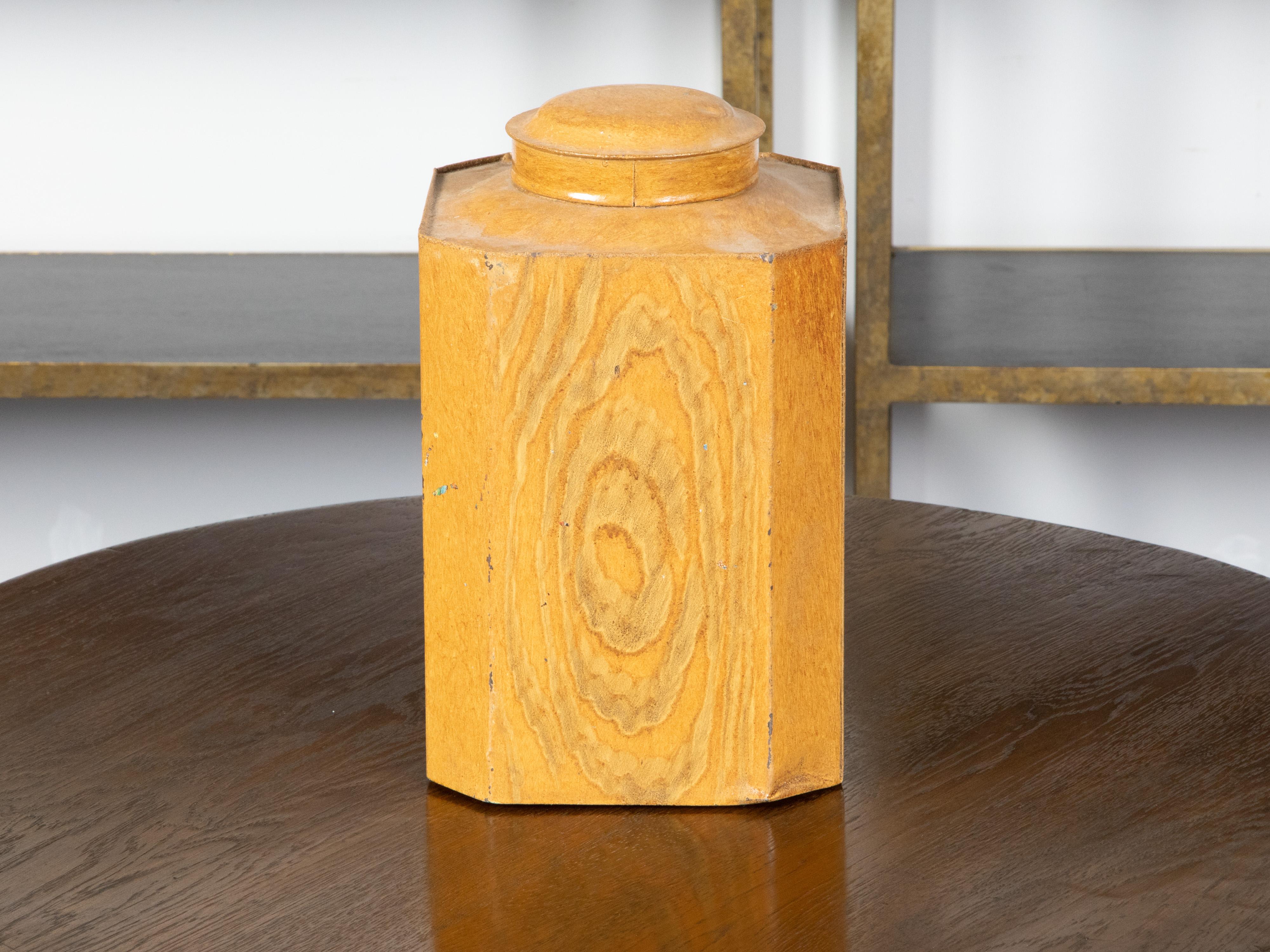 A tin canister from the 19th century, with faux bois finish and canted corners. Created during the 19th century, this canister features an octagonal body adorned with a yellow faux bois finish. Topped with a circular lid, this 19th century tin