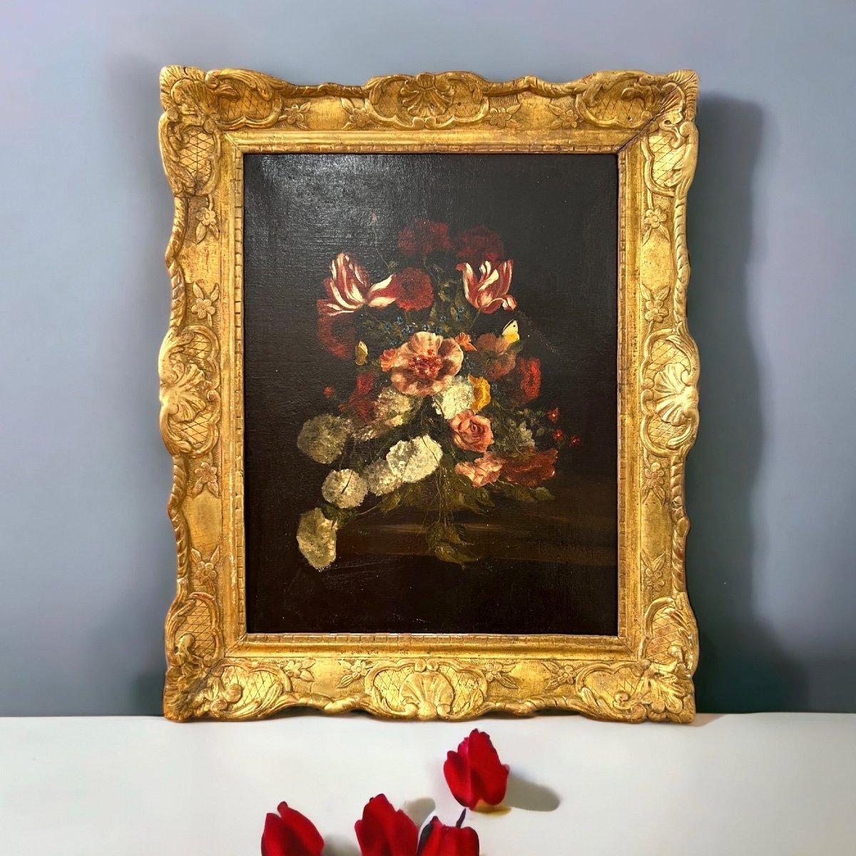 We present you this oil-on-canvas painting representing a refined arrangement of flowers in vibrant colours against a deep-dark backdrop within a splendid 19th-century gilded frame. The frame is enhanced with delicate gold leaf decorative motifs. It