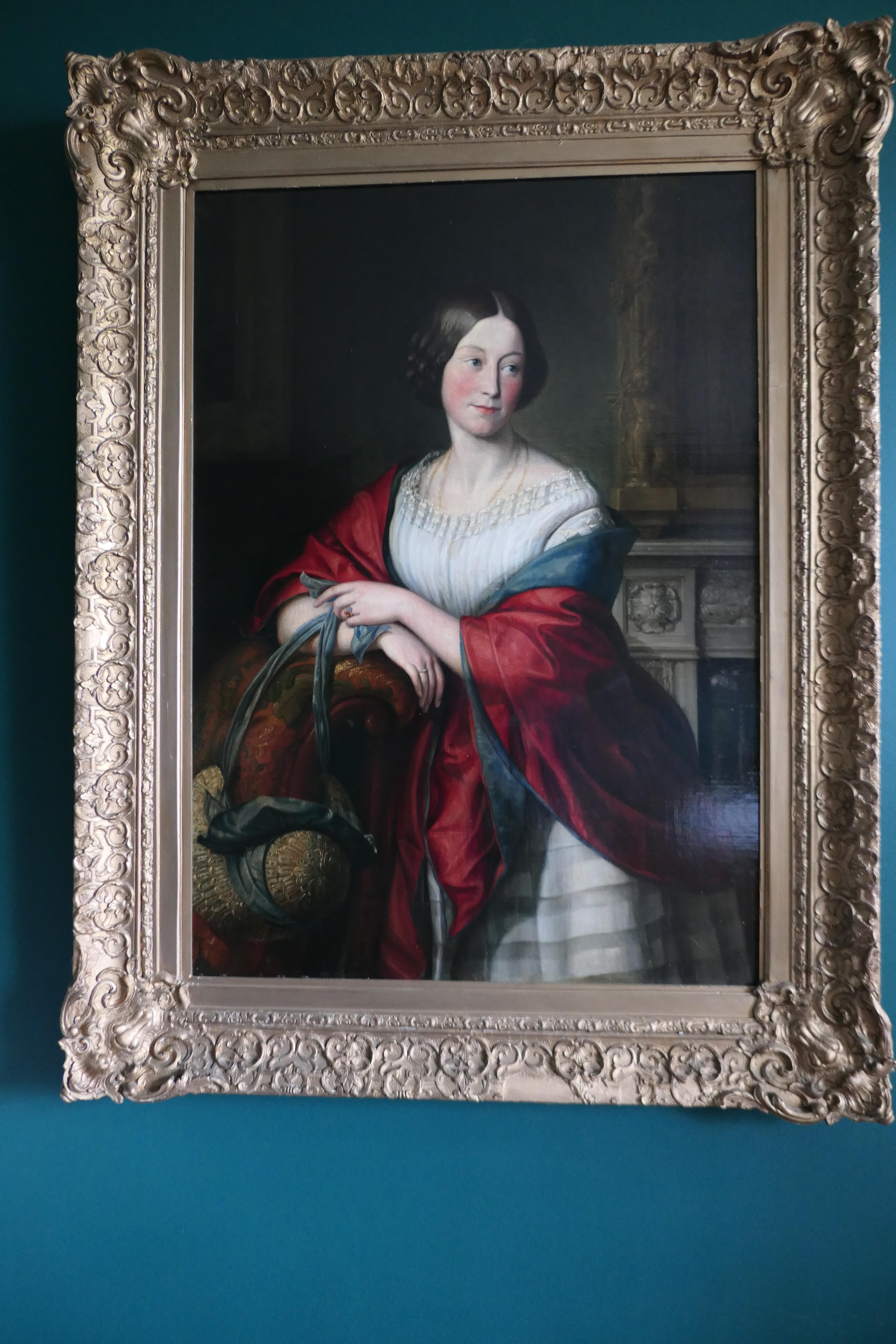 19th century oil on canvas portrait of Mary Harris Stretton, with bonnet and shawl

A Delightful portrayal of a young lady at 35 years of age, she is leaning on the arm of a chair, wearing a bright red shawl and and holding the ribbons of her