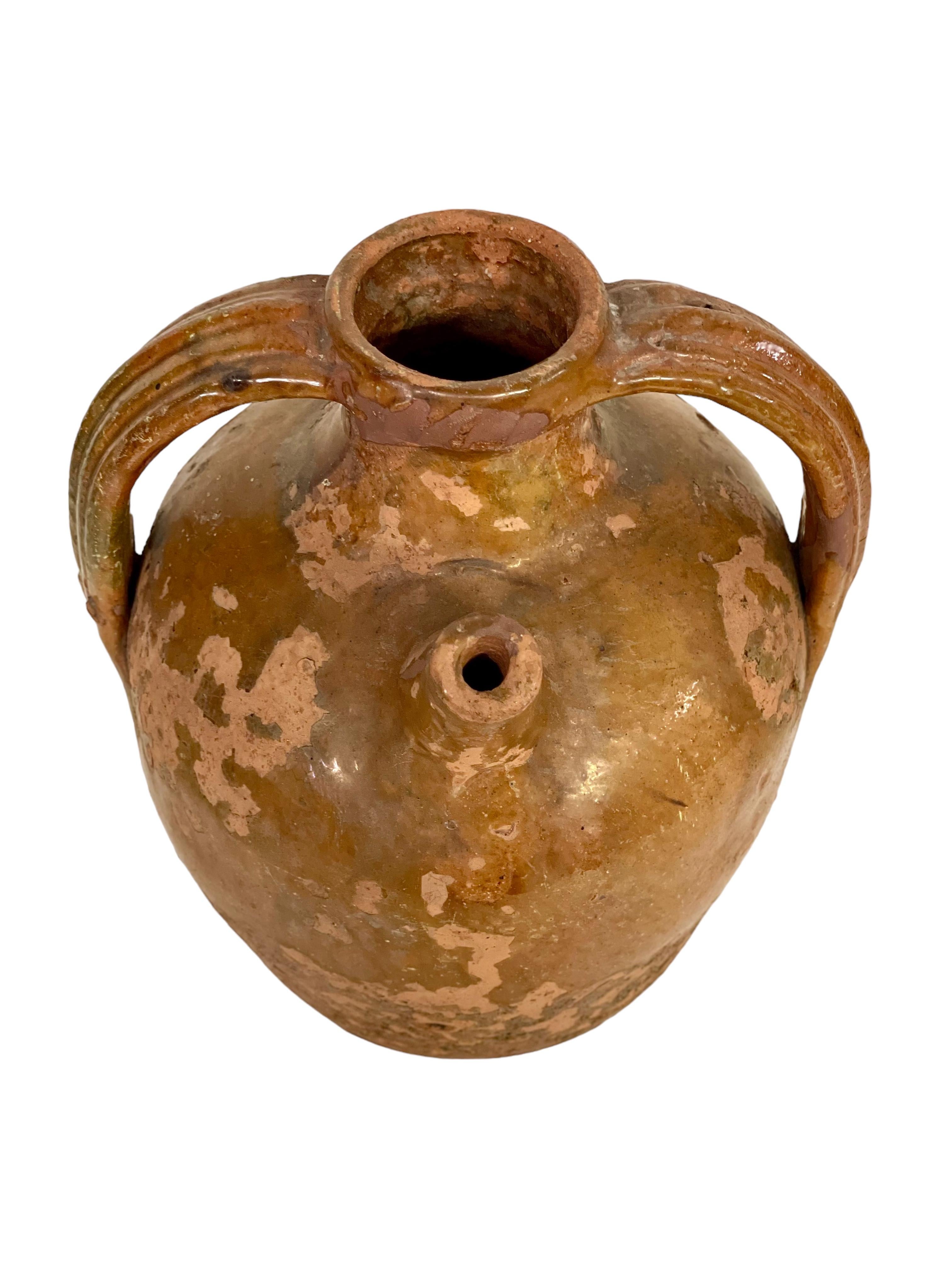 A wonderful antique oil jar, dating from the 19th century, and originating from the South of France. Traditionally shaped, with a short pouring spout and two large side handles, this shapely vessel has been coated with a gorgeous green and brown
