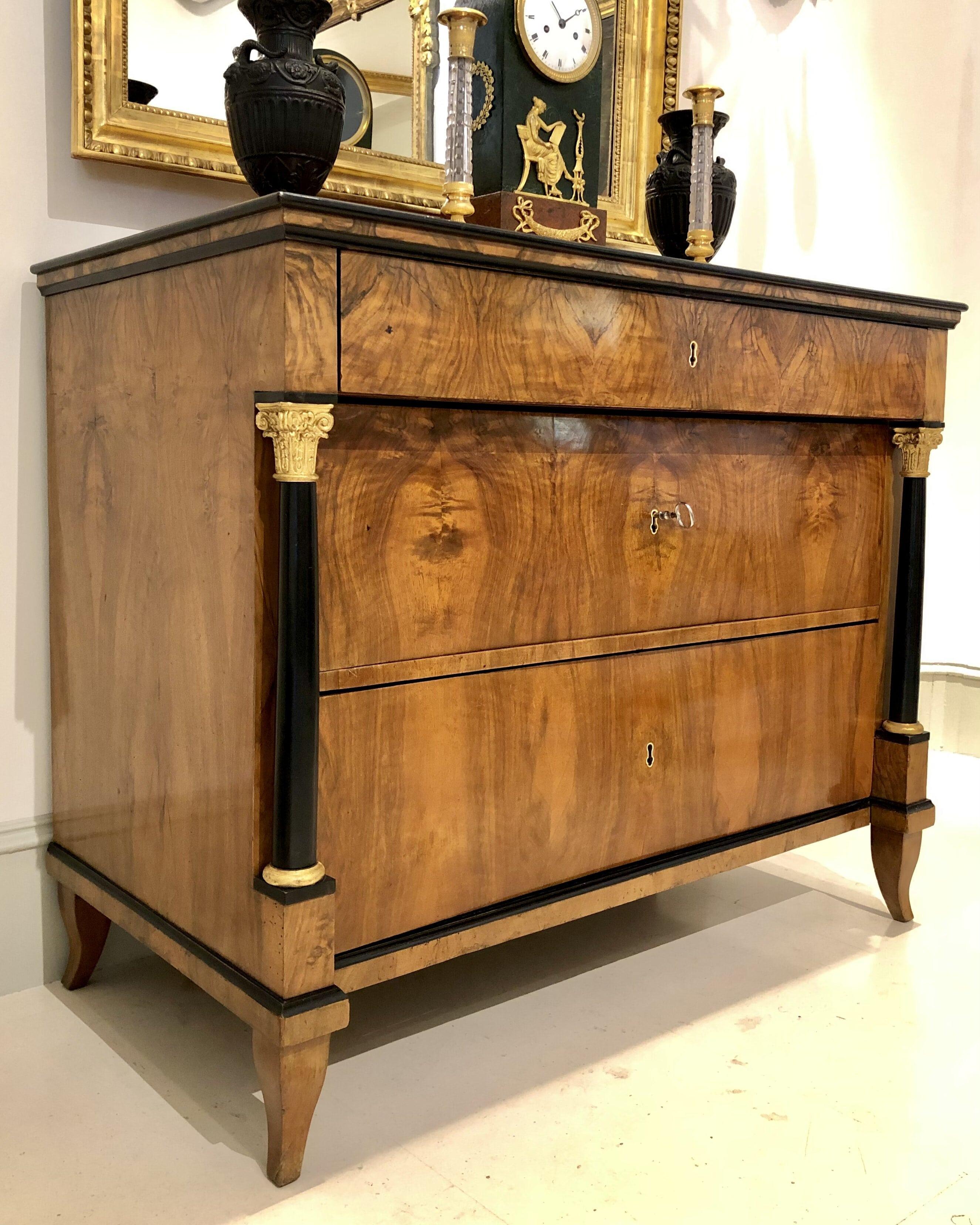 Elegant 19th century Austrian Biedermeier commode in walnut, with bone keyholes, ebonized columns and carved and gilded capitals. Standing on four delicate pointed feet, this Biedermeier commode features three drawers with their original