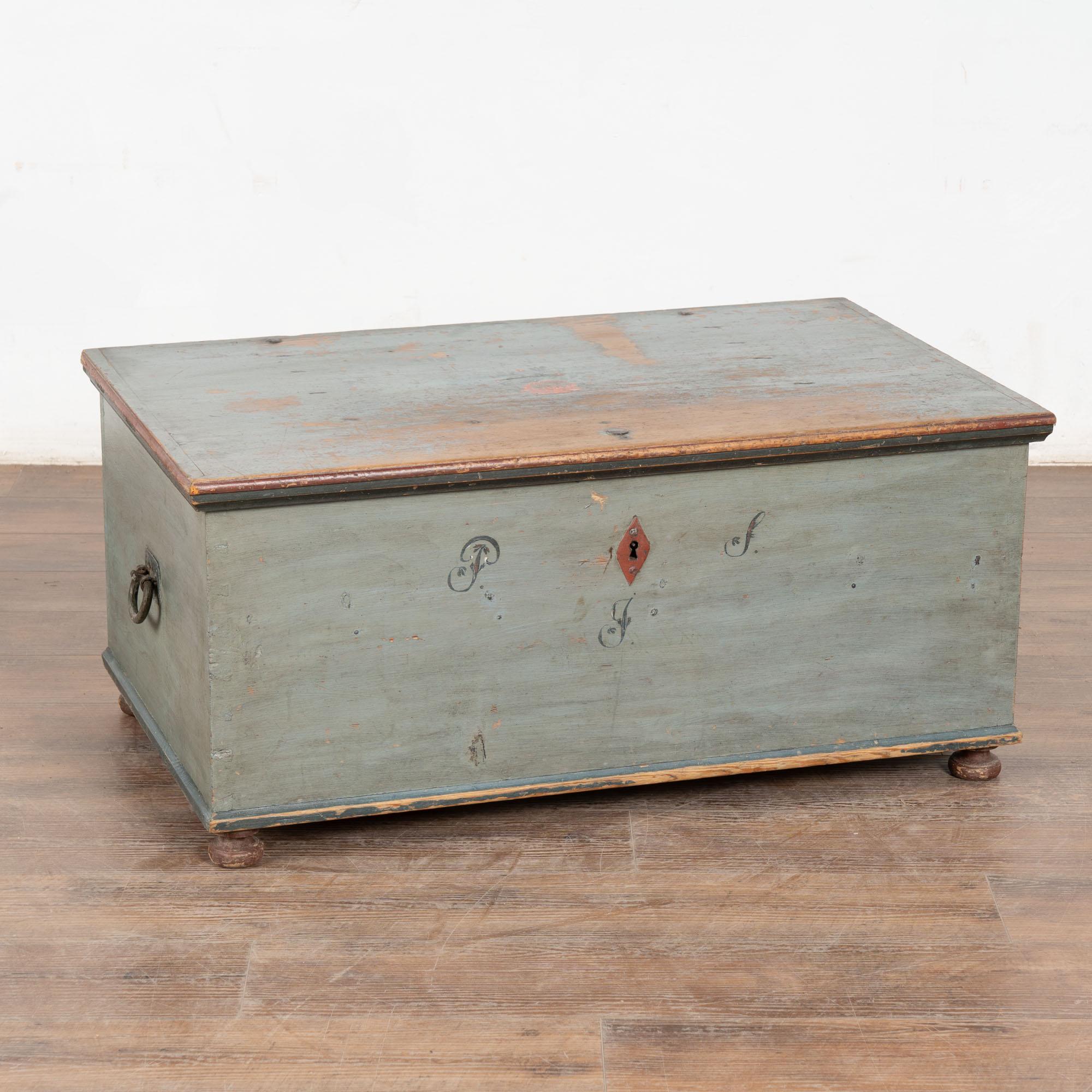 La peinture bleu clair est entièrement d'origine sur cette belle malle à toit plat. Un simple monogramme de trois lettres indique qu'il peut s'agir d'un cadeau de mariage ou de dot.
Cette malle possède des poignées latérales en fer d'origine, de
