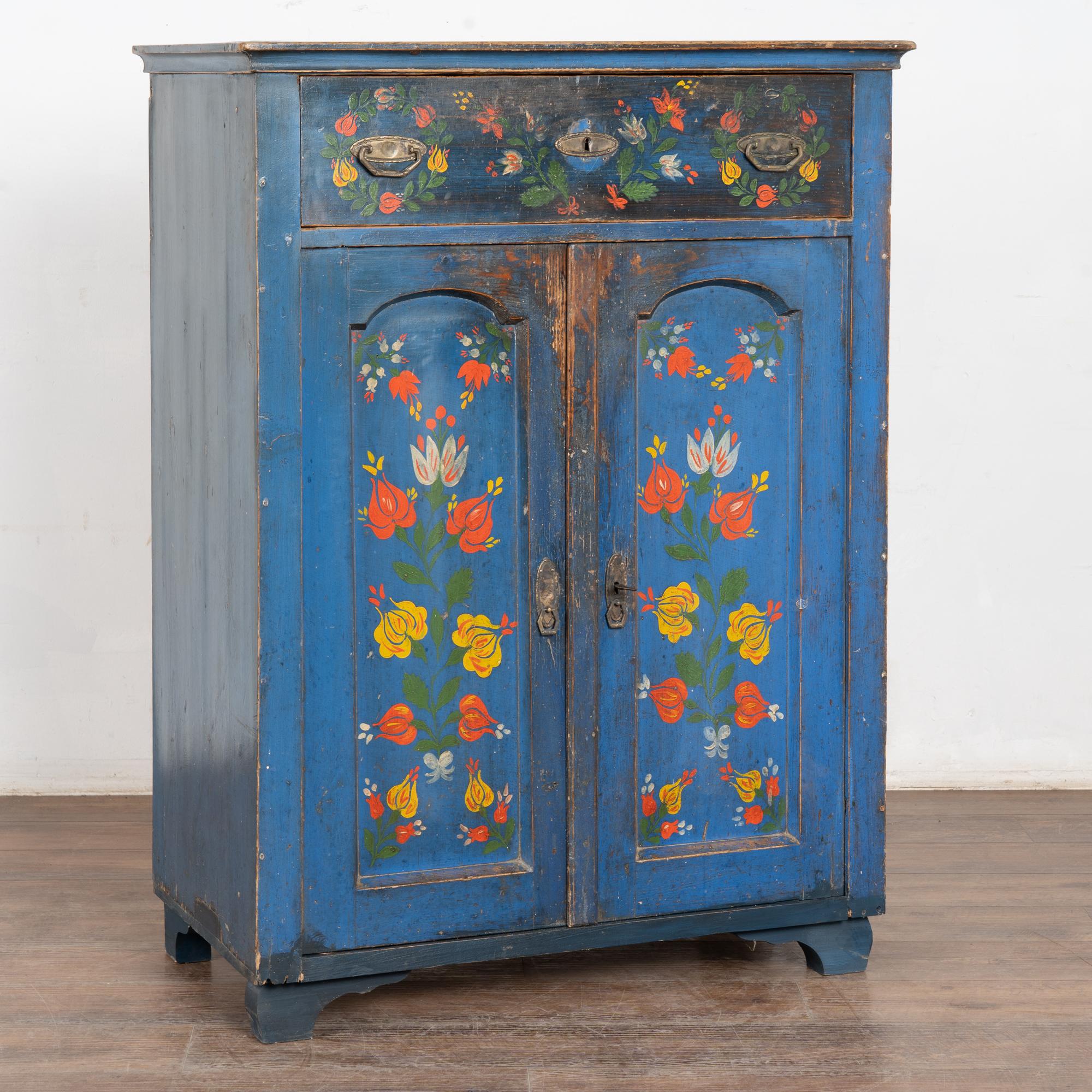 I colori vivaci abbondano in questa originale credenza dipinta con fiori in rosso, giallo e bianco su uno sfondo blu brillante.
Esamina le foto ravvicinate per apprezzare i deliziosi dettagli folk-art dipinti a mano. Le alterazioni della finitura