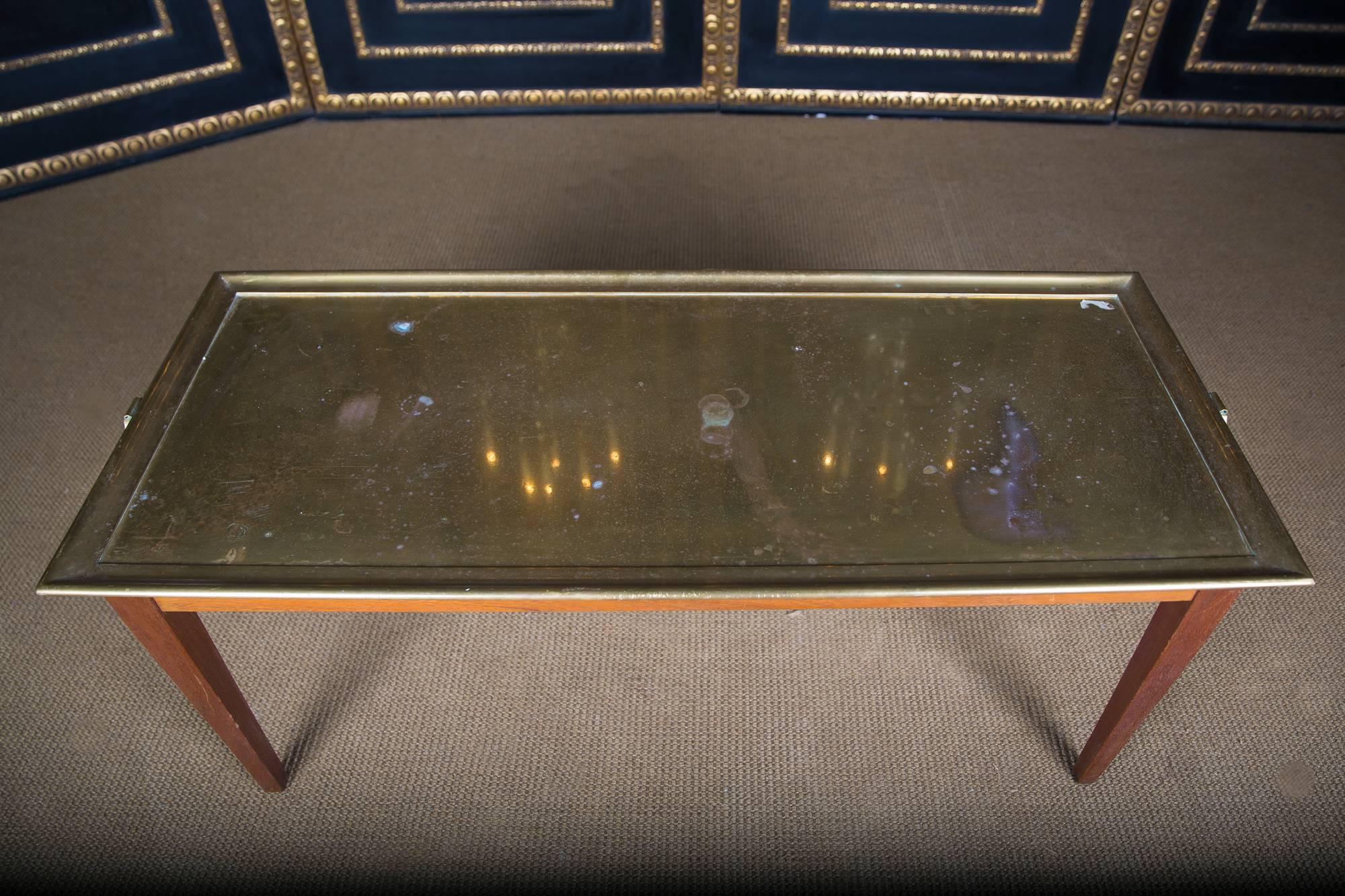 Solid mahogany. Rectangular frame on conical feet. Easily protruding, tabletop made of brass with brass handles on each side. The complete brass plate is removable, similar to a serving trolley / tray.

  