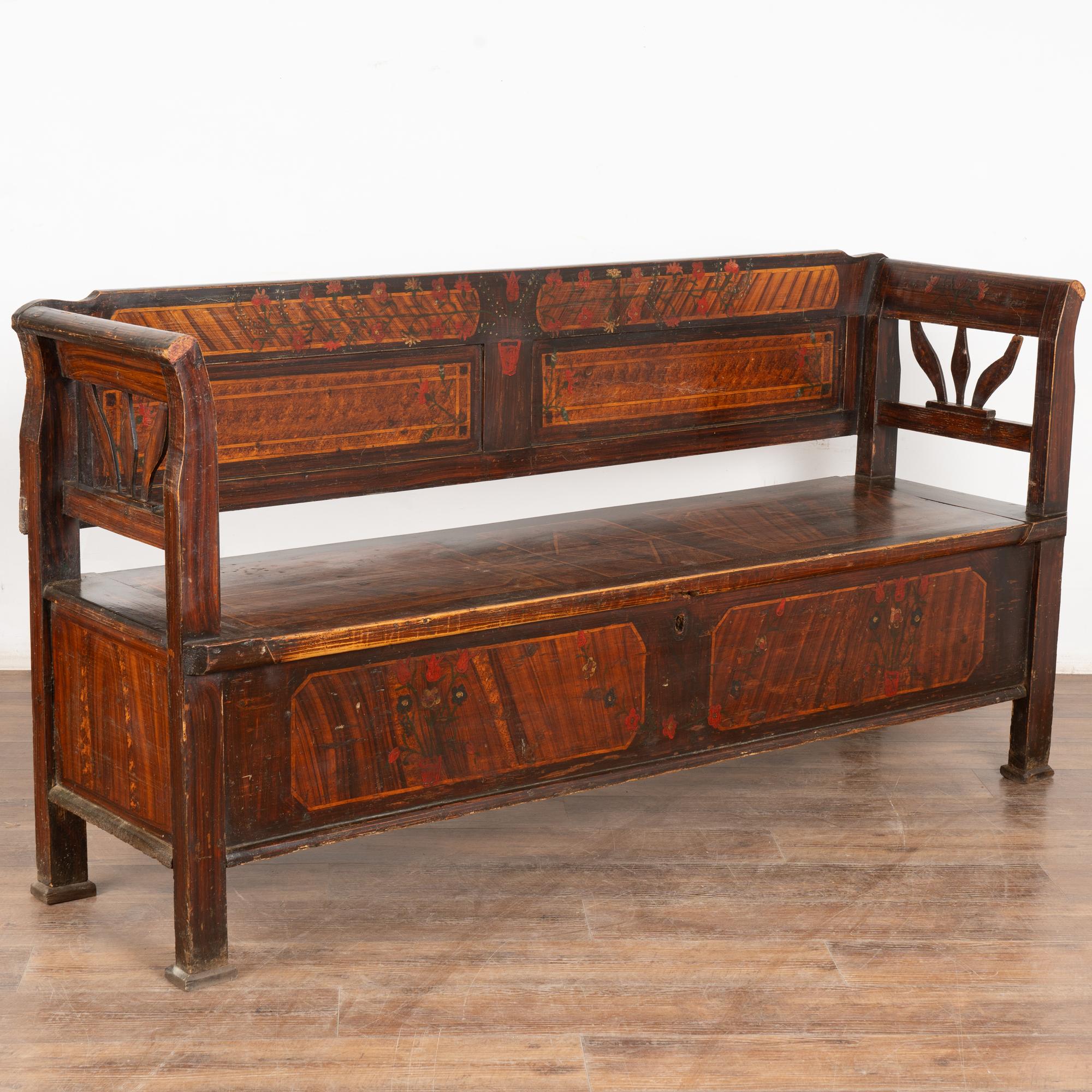 Ce banc en pin, peint à la main, présente un fond traditionnel en faux bois brun et un motif floral.
Dossier solide, accoudoirs légèrement incurvés et banquette rabattable révélant un rangement intérieur (divisé). 
Restauré, nettoyé et ciré, ce banc