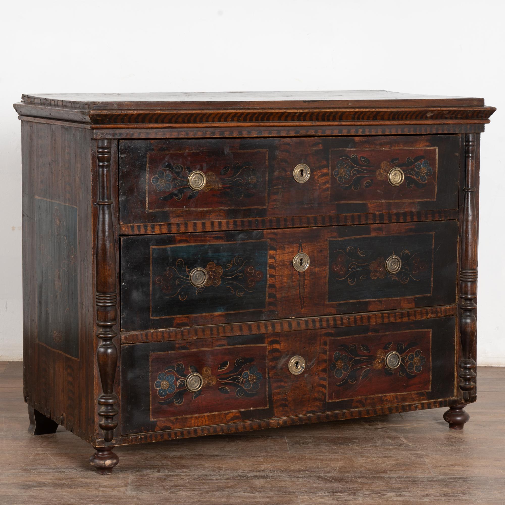 Original hand-painted chest of 3 drawers flanked by half-columns. Hand painted flowers and flourishes seen here were a traditional folk art design of the era set against a brown faux wood finish. Generations of use are revealed in the distress to