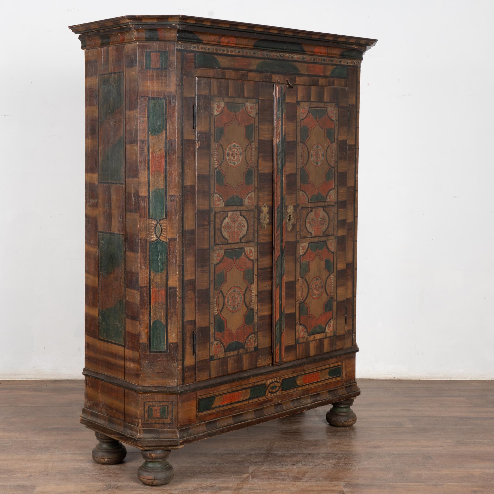 Questo armadio originale dipinto mantiene ancora la qualità e i dettagli della finitura dipinta a mano con uno sfondo unico e colorato. Le sfumature di verde, blu acqua, rosso e marrone sono tutte in mostra.
Un chiavistello esterno tiene le porte in