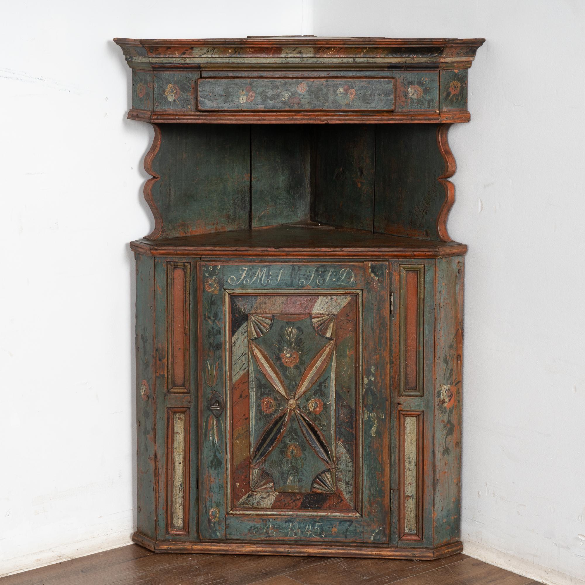 Precioso armario esquinero original pintado, procedente de Suecia, con tonos rojos, cremas y verdes acentuando el fondo azul general con el pino natural debajo, lo que resulta en una pátina atractiva, cálida y envejecida. 
Es probable que este