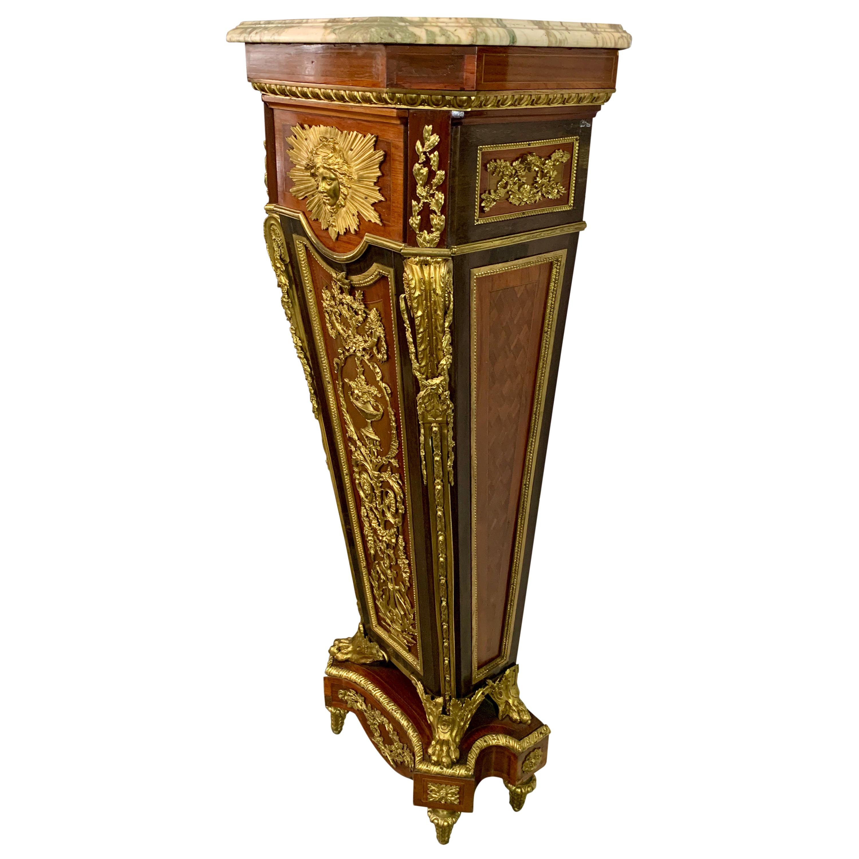 This wall-side gilt bronze mounted pedestal with stepped veined marble top with canted front corners, above the rectangular upper section centred by a Mercury mask and sunburst with crossed lower branches, the angles with an acanthus-cast scrolled