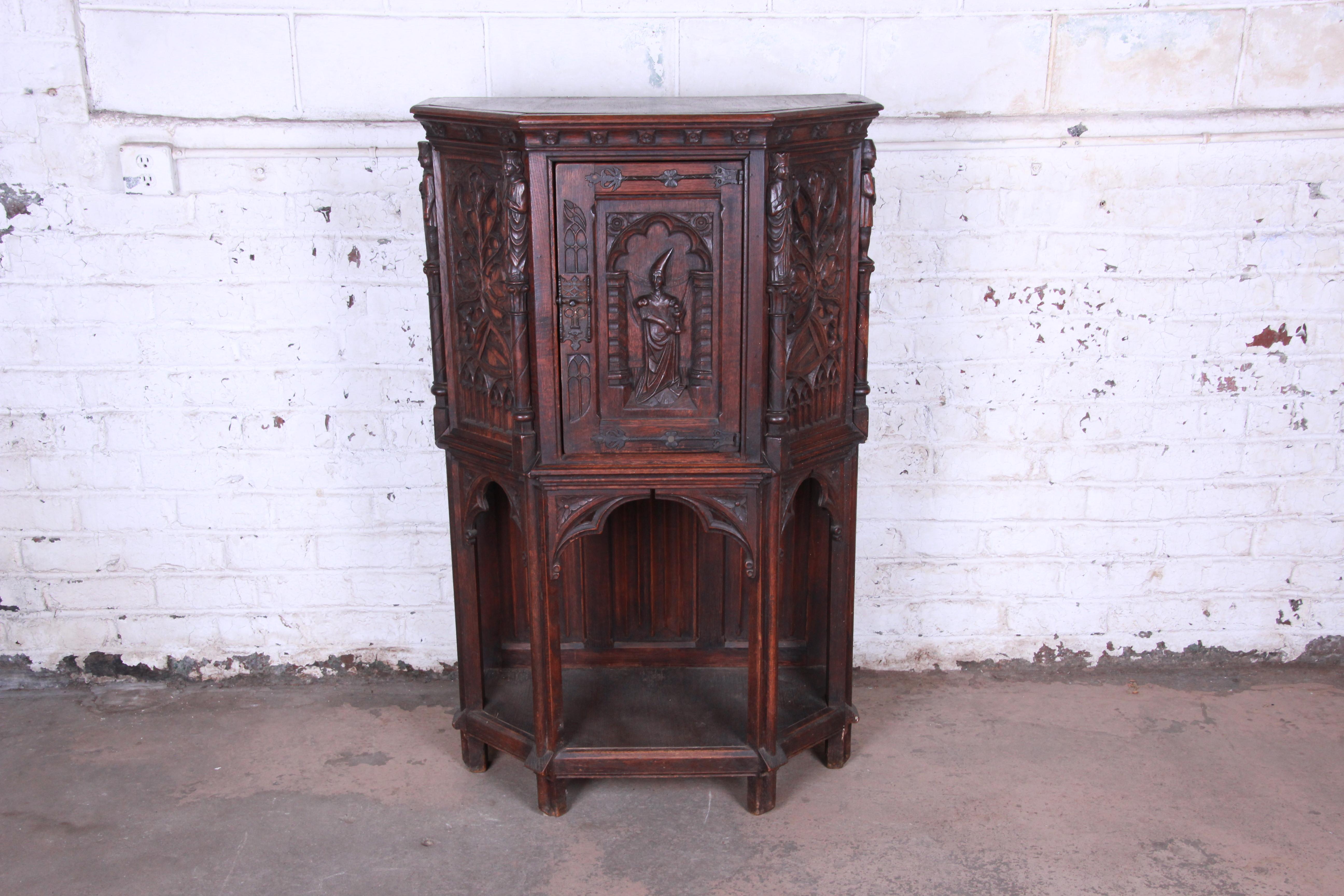 An outstanding 19th century ornately carved oak gothic bar cabinet. The cabinet features solid oak construction, with stunning carved wood details. A single door carved with a young prince or nobleman opens to reveal a shelved storage area for
