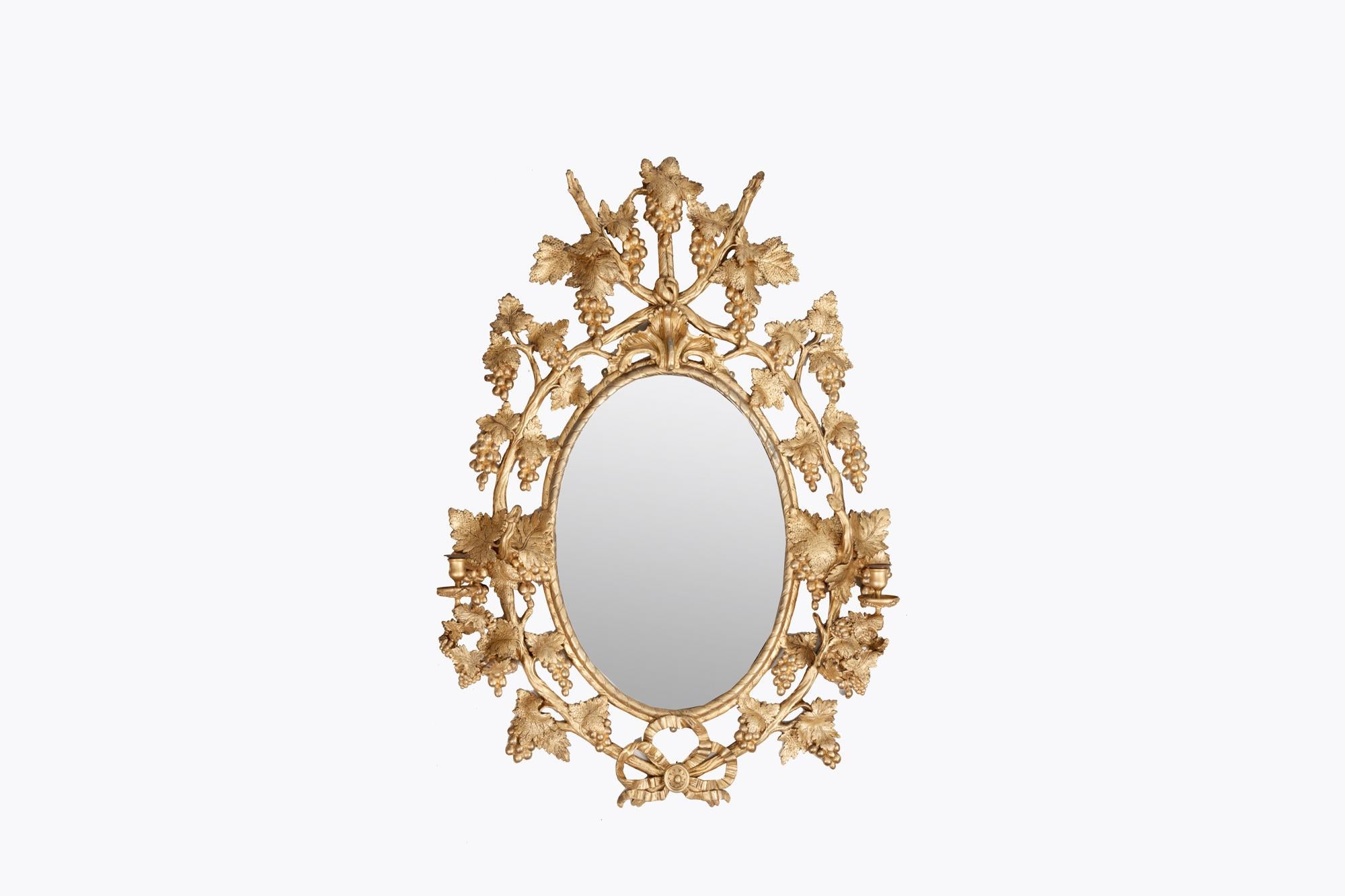 Mid 18th Century Irish carved giltwood oval girandole mirror attributed to John Booker. Boasting a highly ornate carved giltwood border surrounded by vine stock with leaves and bunches of grapes, all connected by a rope tied in a knot to the base.