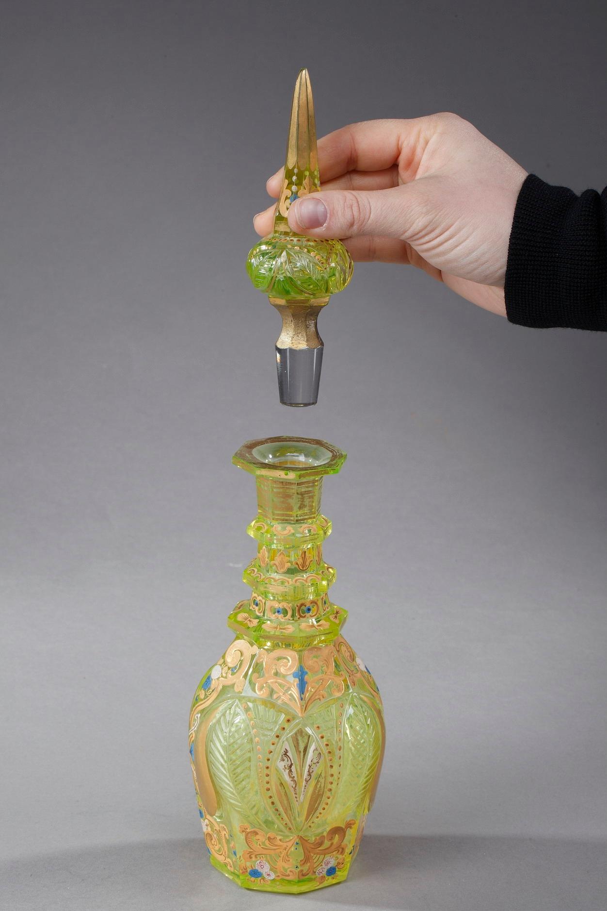 Ouraline glass decanter with its pointed stopper, decorated with painted and enameled foliage, arabesques and floral motifs. Three interspaced rings adorn the collar while floral and geometrical patterns highlight the paunch. Bohemia for the East,