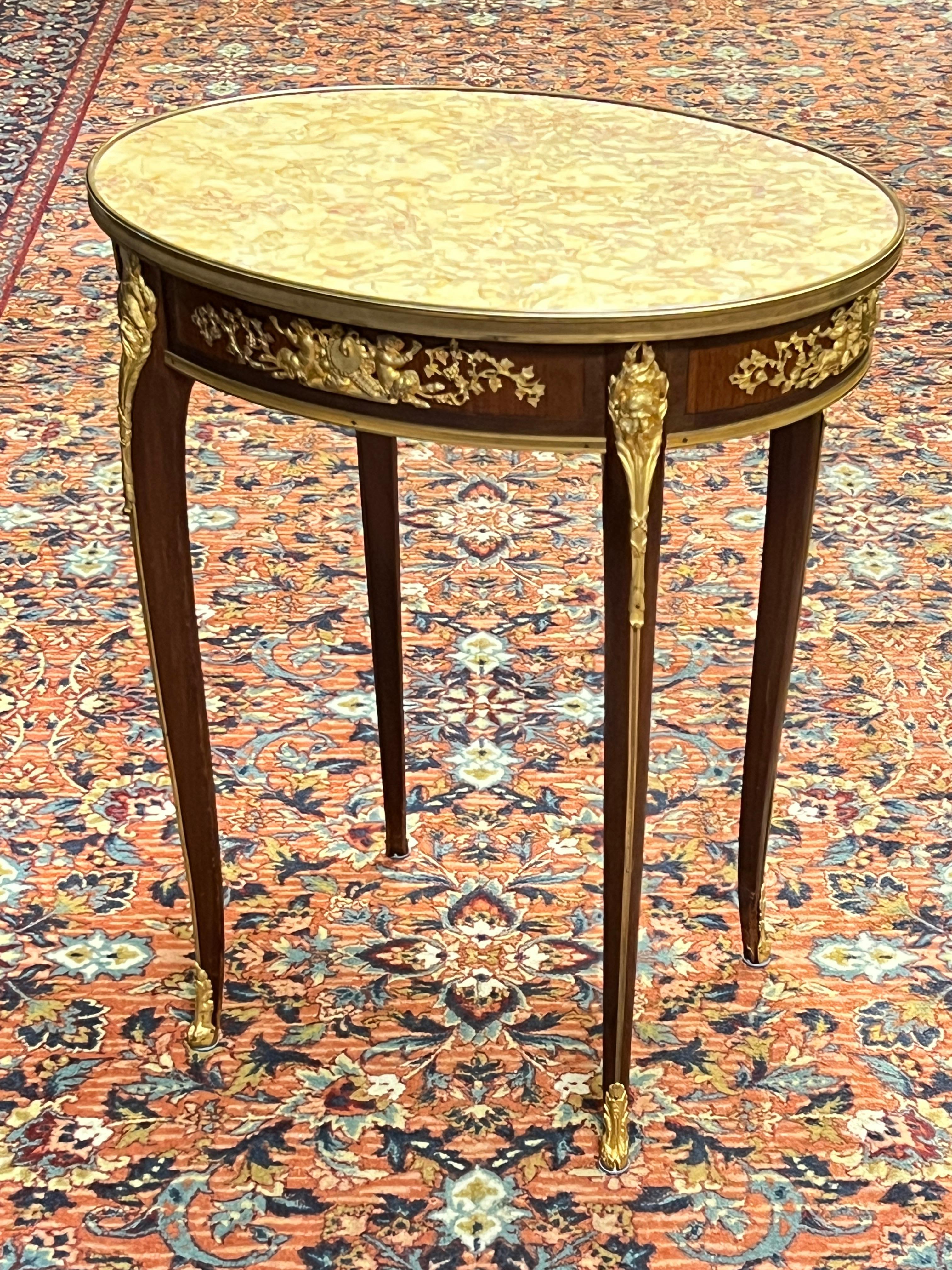 Exceptional antique (19th century) oval shaped occasional or side table in French Louis XV / XVI style, with variegated Valenzia (ie. Valencia) marble top, mahogany and fruitwood veneers, and 
gilt bronze mounts including Bacchic masks at the tops