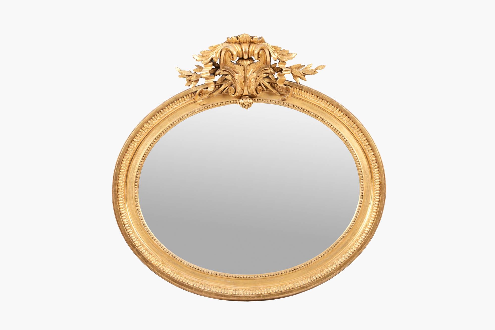 19th Century oval gilt mirror. The frame is carved with an egg and dart design alternating with convex fillets and an inner gilded beaded loop. At the top, the frame is decorated by a large cartouche featuring acanthus leaves and ribbon scrolling.