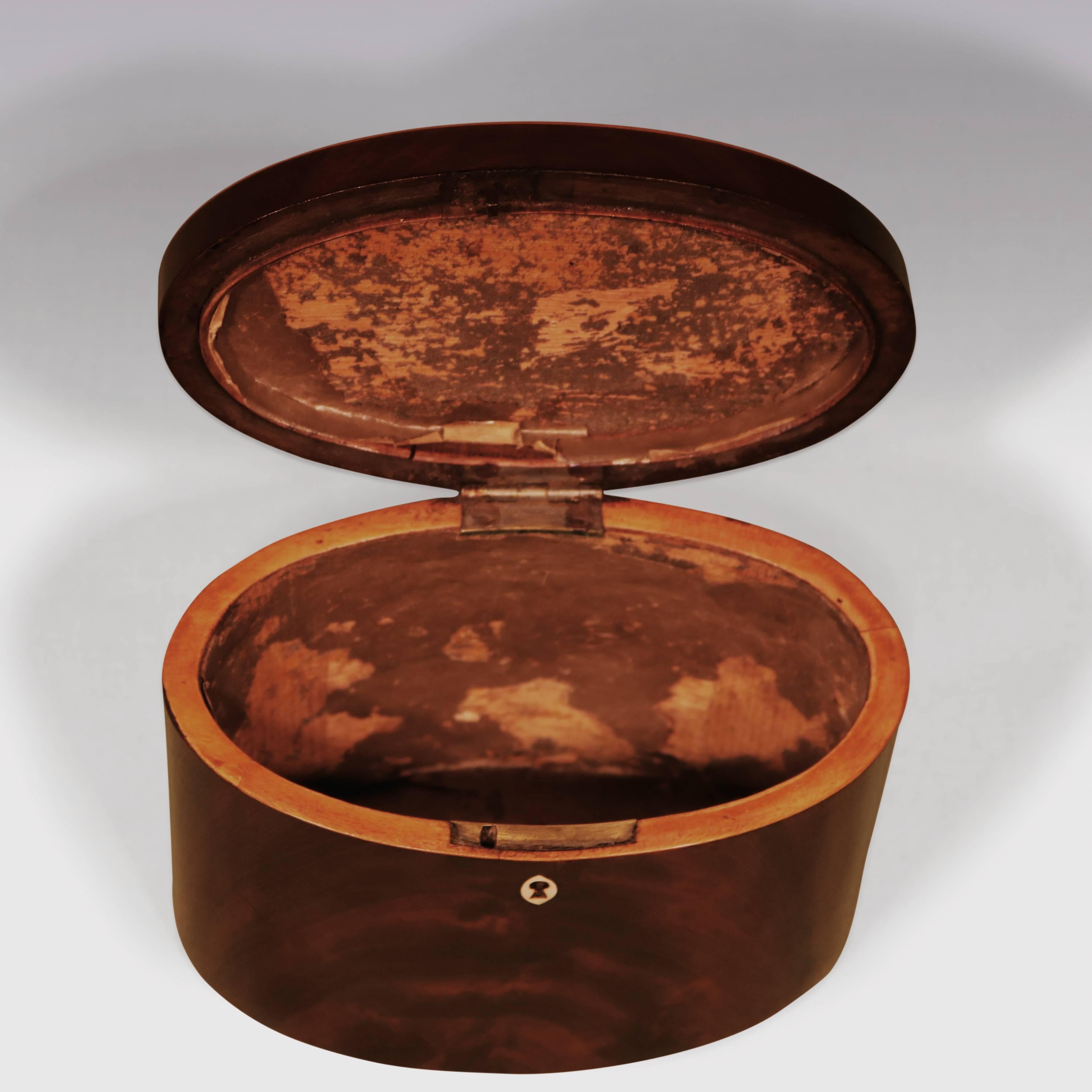 A small late 18th century oval shaped flame figured mahogany and boxwood strung tea caddy, retaining original brass axe-head handle.