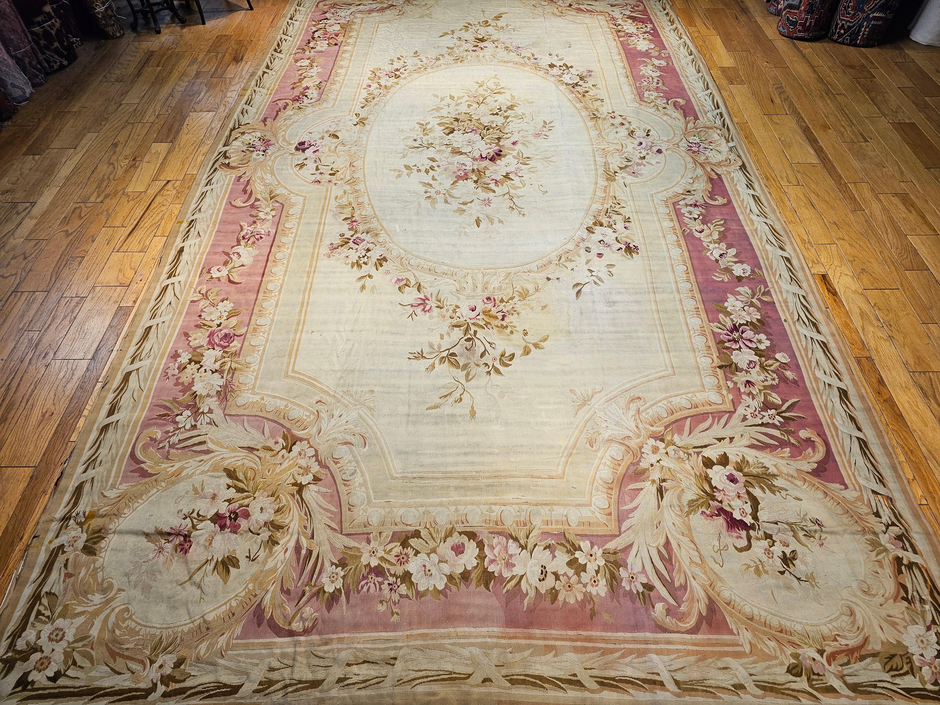  19th century French Aubusson oversized rug in a floral pattern in ivory, red, pink.   A central oval floral medallion flanked by sprays on the ivory field is within a pink color border with floral design throughout.  The Aubusson carpet has a