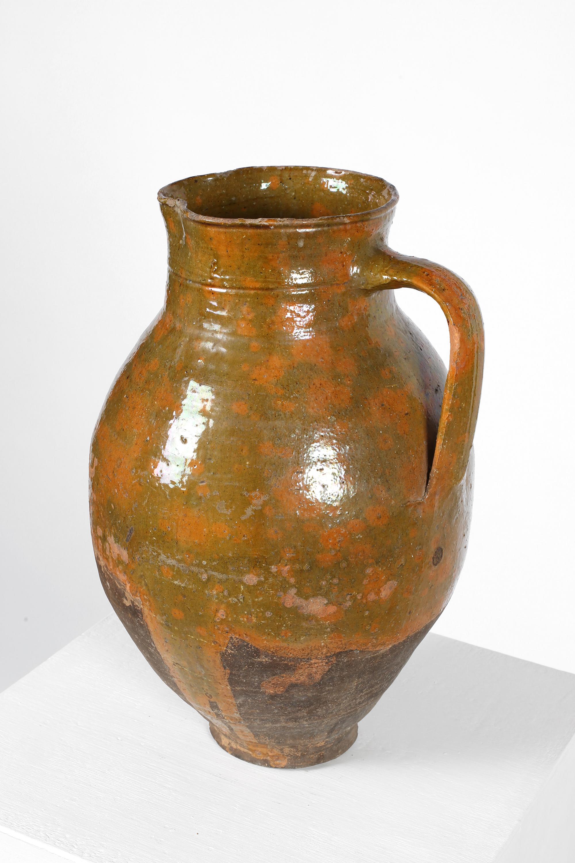 A 19th century oversized earthenware wine pitcher from Catalonia with mottled olive green/ochre part glaze. The exaggerated scale suggesting that it was likely used in a restaurant, rather than domestically. Spanish, c. 1850.