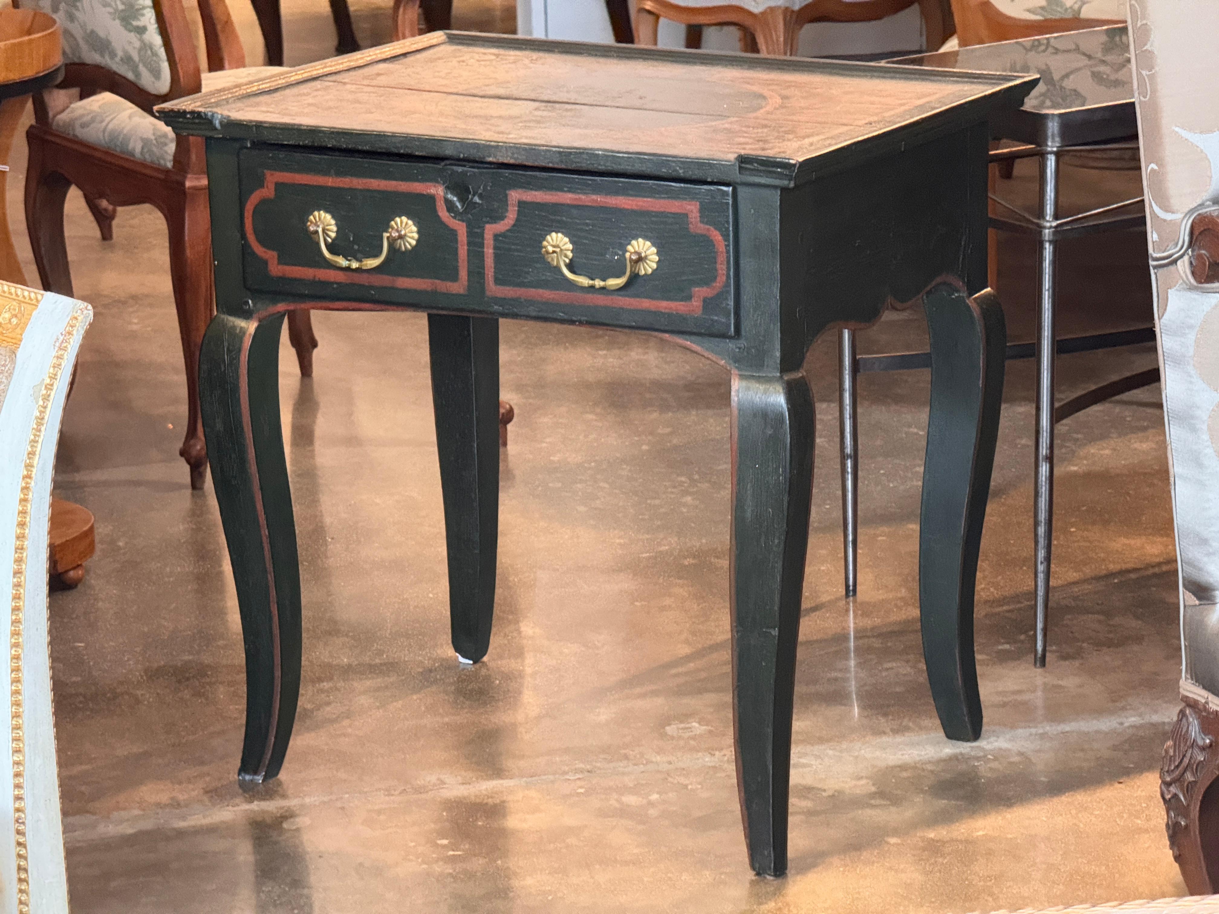 Table with a shaped apron and cabriole legs, featuring paint-decorated borders and a bold circular motif on the top surface, as shown in the close-up image. The two-drawer front includes painted surrounds framing brass pulls. Wear to the painted top
