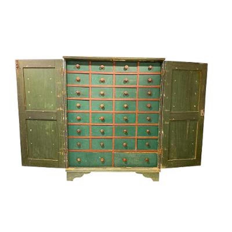Thirty drawer 19th century apothecary chest in green paint, having seven rows of four drawers above a pair of drawers. The green painted drawers with red painted pulls and framing all behind a pair of locking, raised panel, removable doors. The case