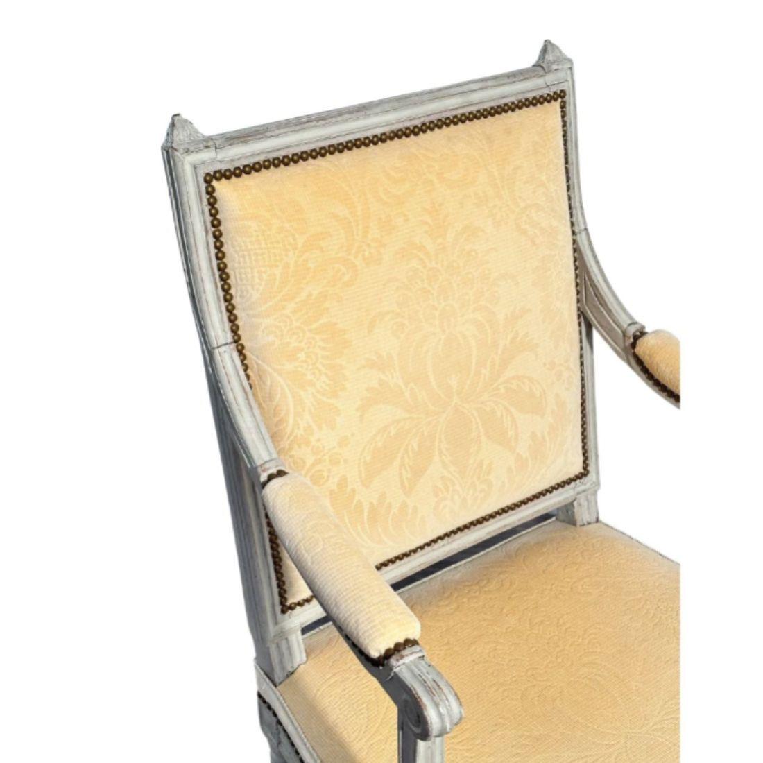 A 19th Century painted fauteuil with yellow damask fabric.  The straight backed arm chair has two finials at the two top corners, padded armrests and carved and fluted frame and legs.  The fabric is finished with nail head trim.  The chair seat has