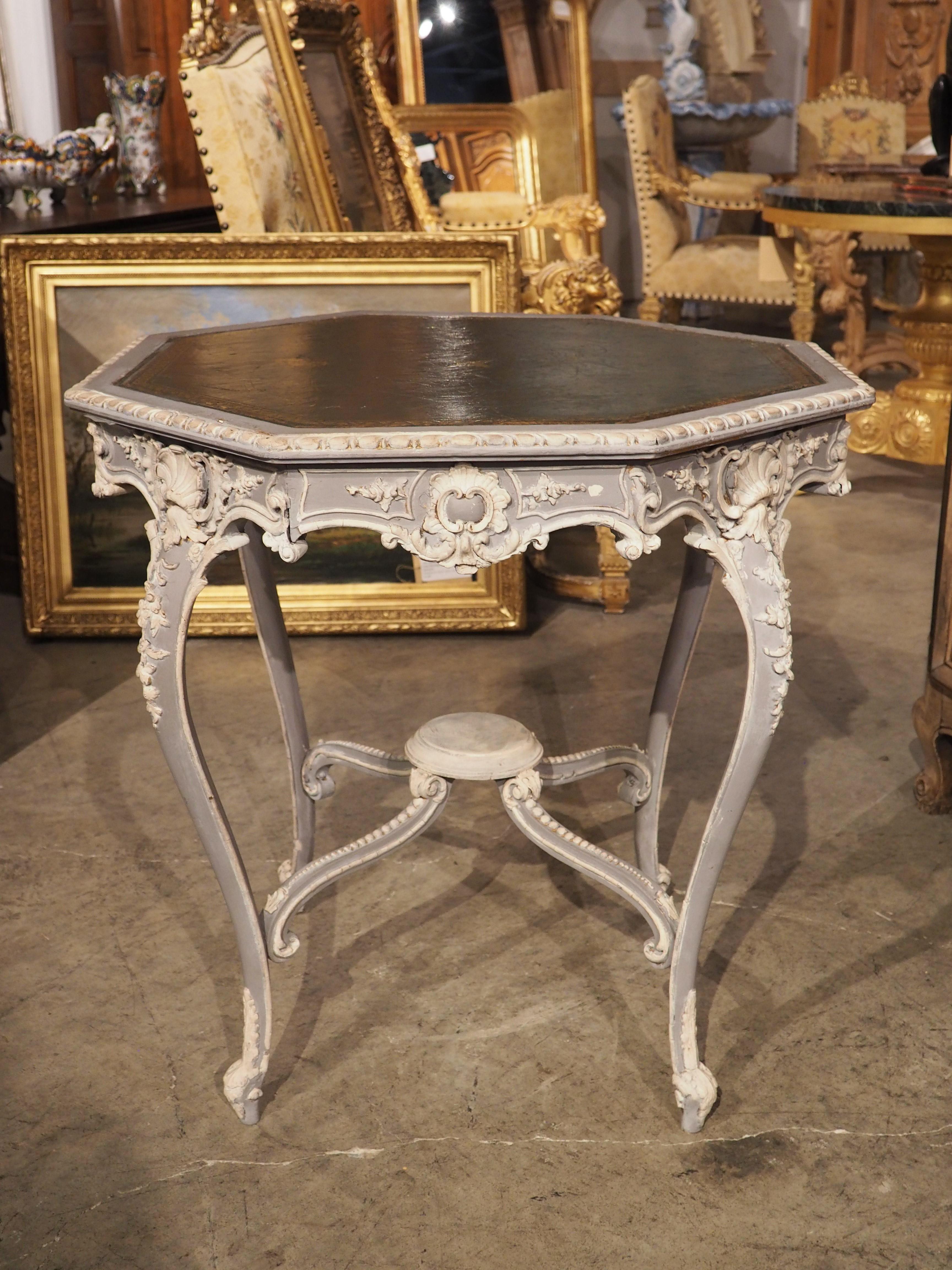 A beautiful example of Louis XV style, this painted side table with leather top was hand-carved in France during the latter half of the 1800’s. The octagonal top table has been covered with a deep green leather that has been adorned with a gold