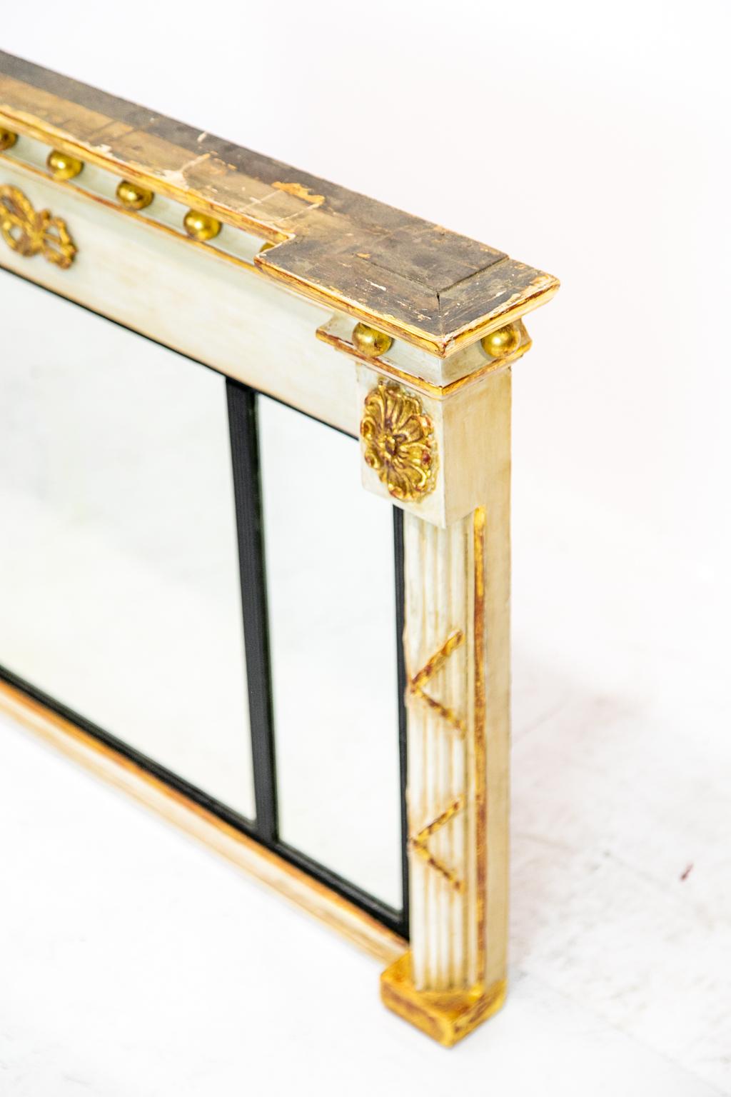 19th century painted over mantel mirror, this striking over mantel mirror has ebony liner around the mirror and is flanked by reeded columns. Gilt balls and medallions grace the top. It has three panels of beveled mirrors.