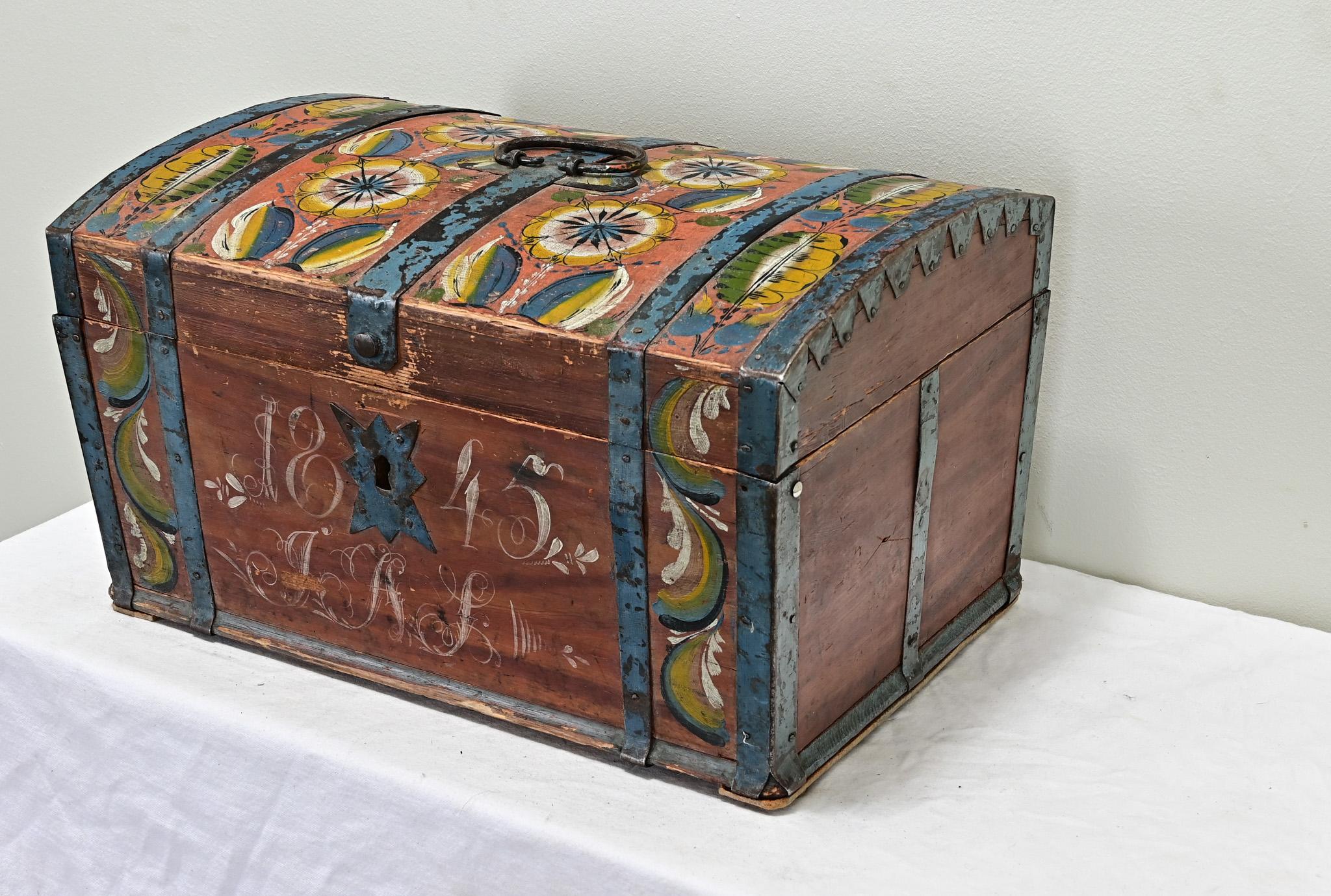 Un piccolo baule matrimoniale da tavolo dipinto proveniente dalla Svezia. Questo baule colorato e allegro ha uno sfondo in faux bois dipinto di rosso con decorazioni floreali dipinte sulla parte superiore e frontale, con monogramma 