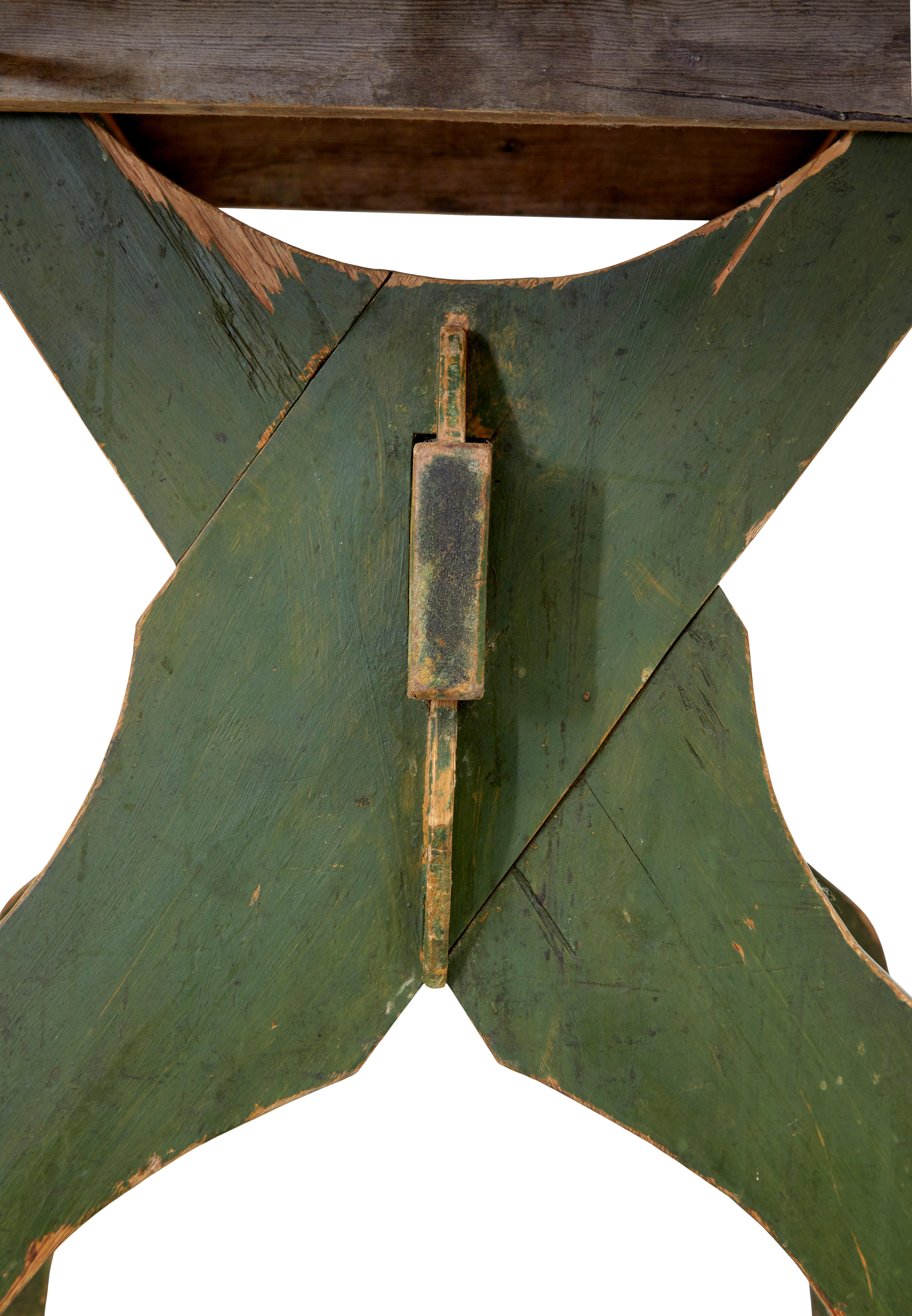 Insolite table rustique en pin suédois vers 1880.

Dessus amovible à 3 planches avec coins arrondis.  Elle repose sur une base en forme de cadre en x avec peinture d'origine, maintenue en place par un châssis et des chevilles.

Idéale comme table