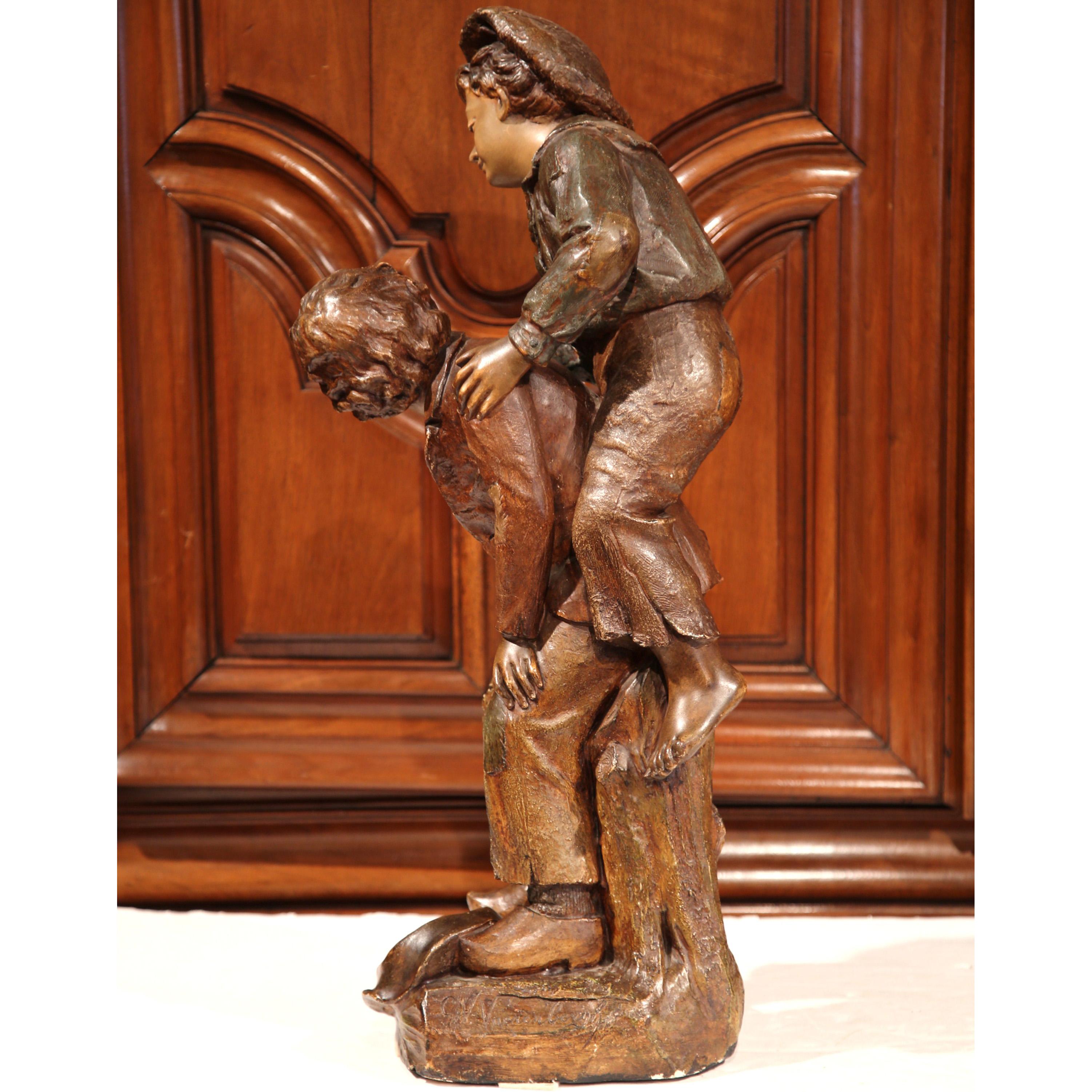 This tall antique terracotta composition was crafted in Belgium, circa 1890. The sculpture, signed on the side G. Van Vaerenbergh with the number 246, depicts two expressive, young boys in rustic clothing, one carrying the other on his back. The