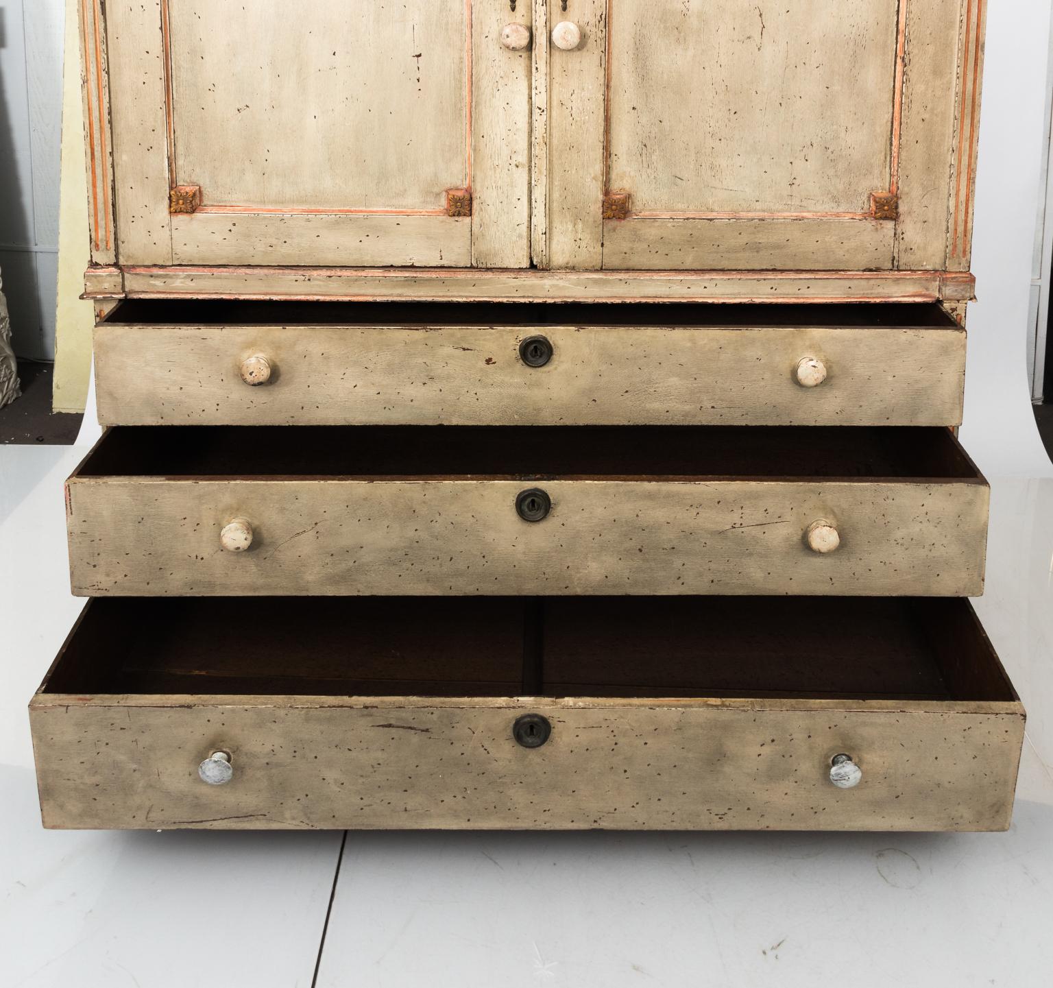 Swedish Gustavian style painted cabinet with three bottom drawers used for storage of linens, circa 19th century. The piece features an angular pediment and painted Roman swags of ribbons throughout. Original brass metal hardware is also delicately