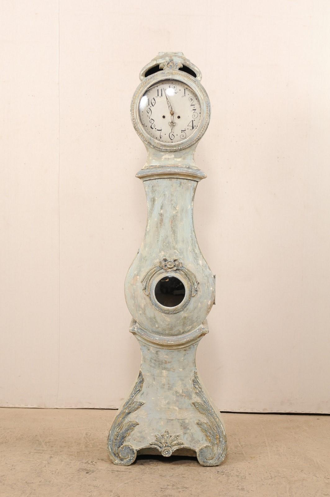 A 19th century painted wood Swedish long-case clock with distinct curvy rain-drop shaped belly. This antique floor clock from Sweden has an elongated arch crest, with hollowed area between the the top of the head, carved at center with floral