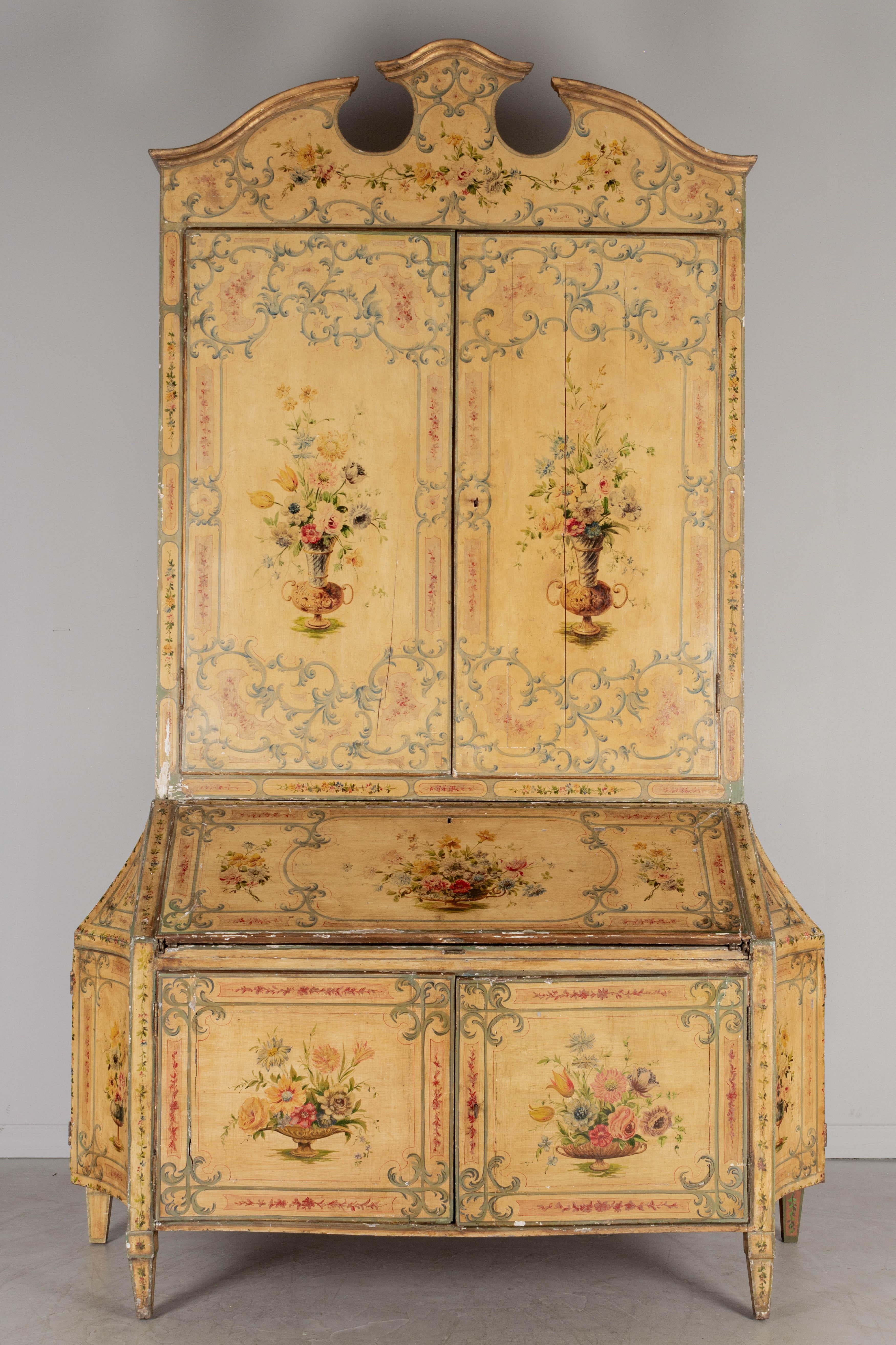 An early 19th century Baroque style Venetian polychrome painted pine tall secretary, in two parts with a tall bookcase and a slant front drop leaf desk. Beautifully hand-painted with floral bouquets and garlands framed by scrolling cartouche motif.
