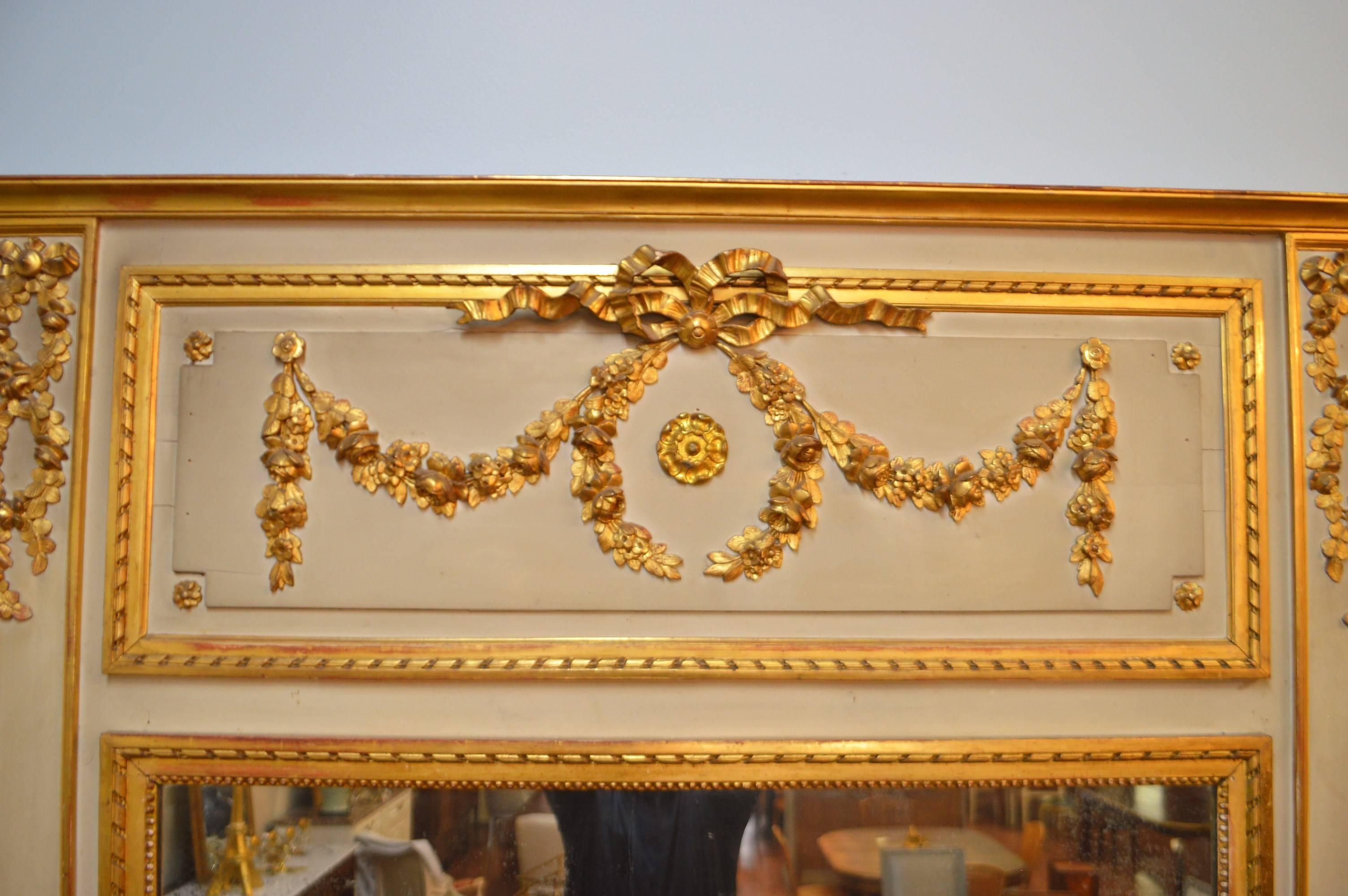 Louis XVI style trumeau mirror from France, good patina on the putty color paint. The gilded details representing hand-carved wreath of flower and acanthus leaves and the typical Louis XVI style rope carving around the inner frame.
The mirror is
