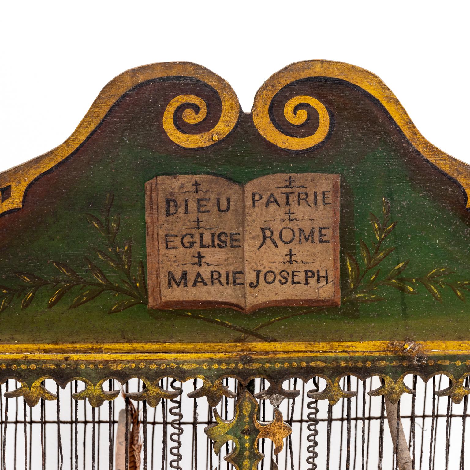 Circa 19th century painted wood and wire birdcage painted in green with gold painted trim with two doors. The top of the birdcage is constructed with a broken scroll pediment detailed with a book and olive branch motif. The book is further painted