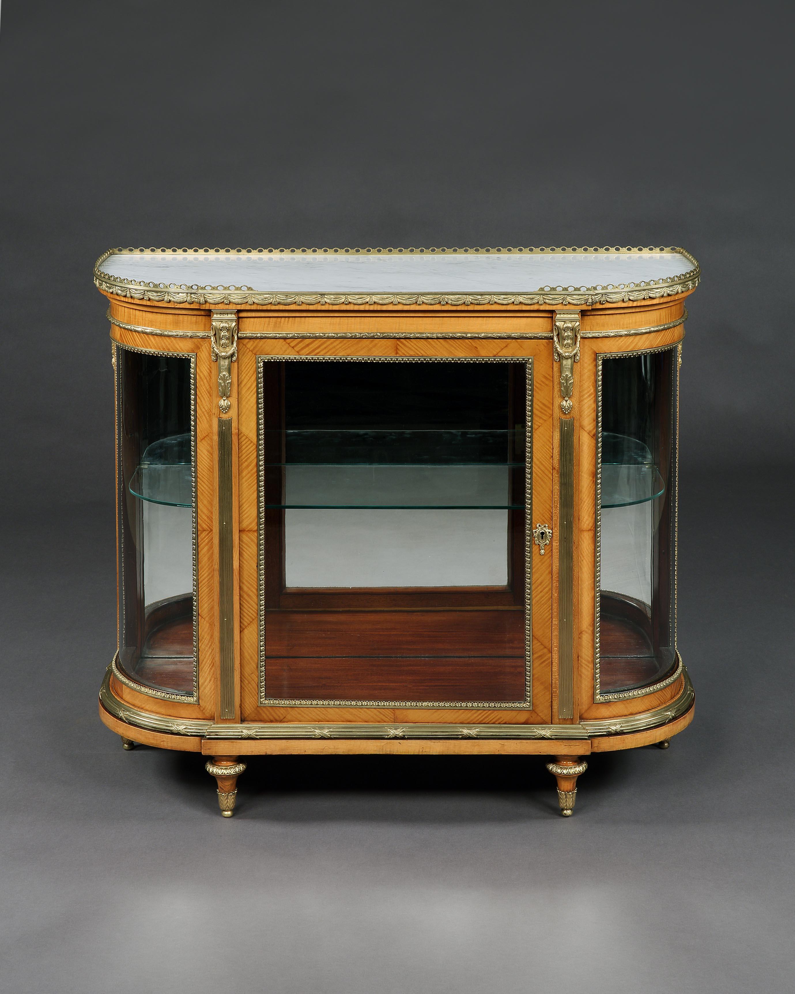 A pair of display cabinets
By C. Mellier & Co.

Constructed in fine satin birch, the demi-lune display cabinets having a gentle breakfront form, and rising from toupie feet, the glazed facets enclosed within ormolu stiff leaf moulding, the