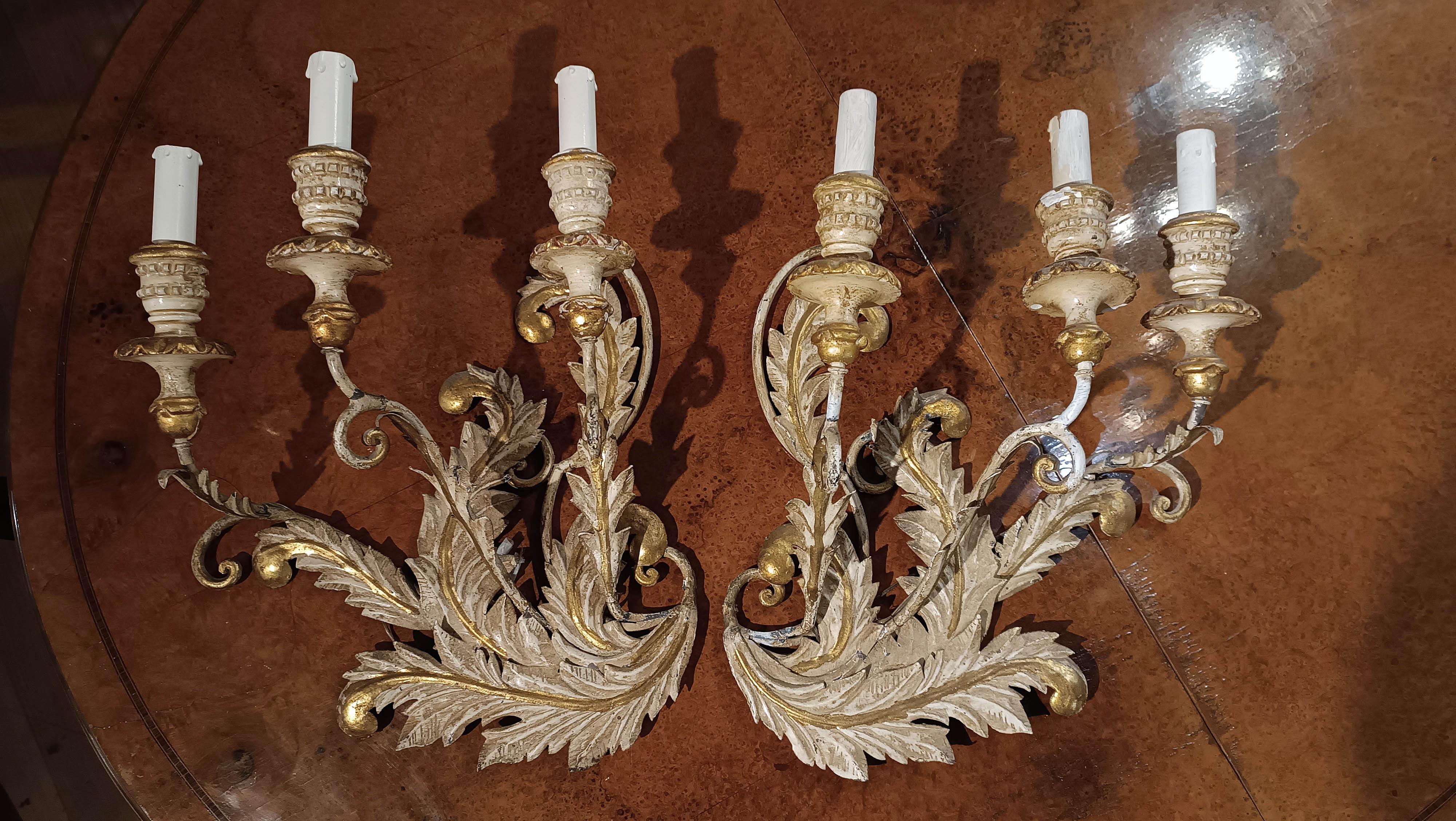 Splendid and refined pair of lacquered and gilded iron wall sconces, each with three lights. The candle holder buds are made of lacquered and gilded painted wood, finely turned to add a touch of elegance. The bodies and arms of the sconces are