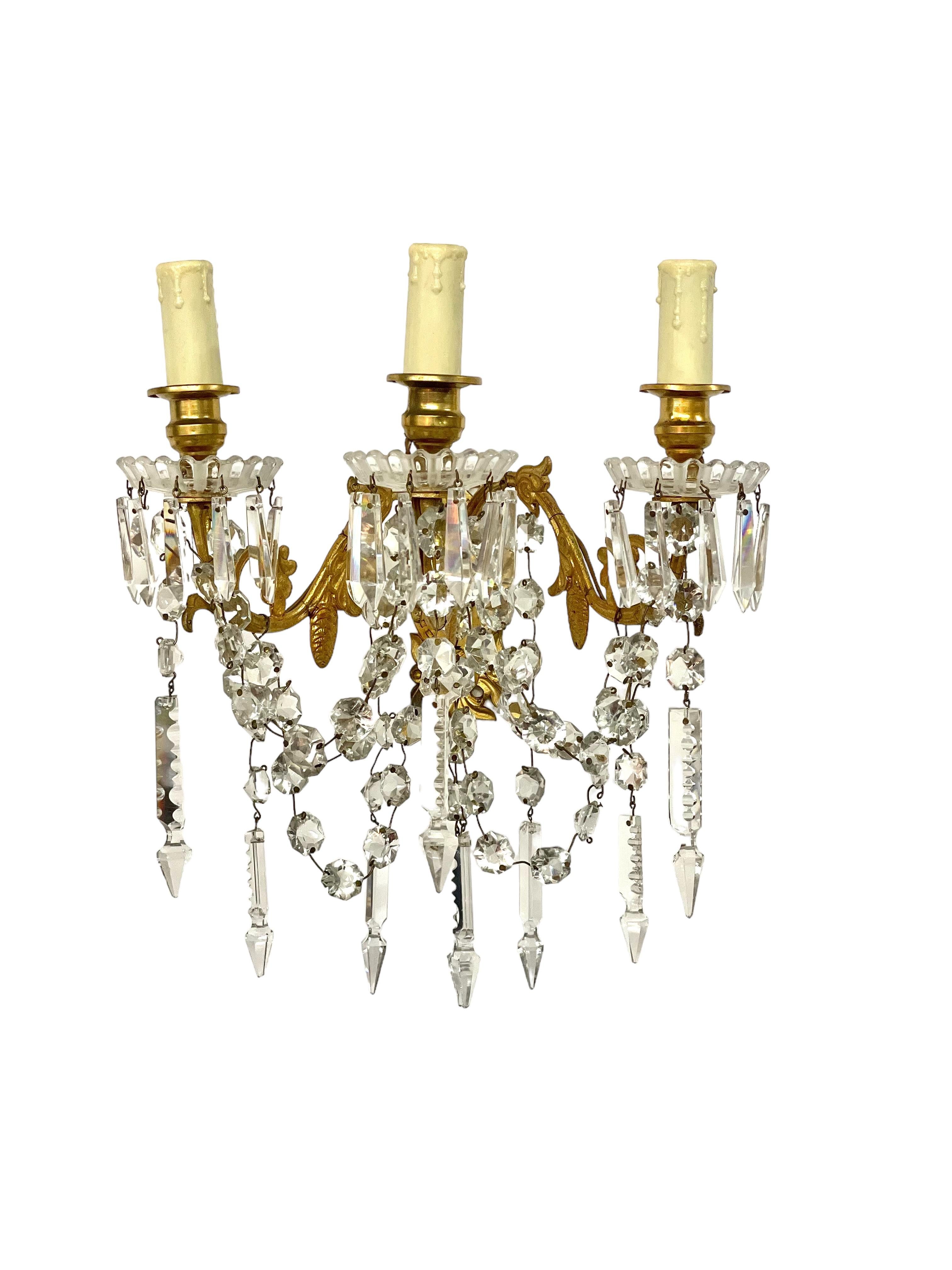Une paire d'appliques scintillantes à trois bras, fabriquées par le célèbre cristallier Baccarat au XIXe siècle. Ces fabuleuses appliques sont fabriquées en bronze doré et sont ornées de pendentifs en cristal taillé et de guirlandes étincelantes. La