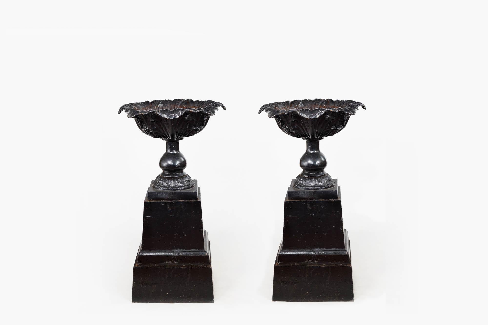 19th century pair of black cast iron urns with baluster pillars and unusual cabbage leaf tops sitting on solid tapering squared bases. The detailed leaf patterns decorating these urns create an organic scalloped naturalistic edge, which contrasts