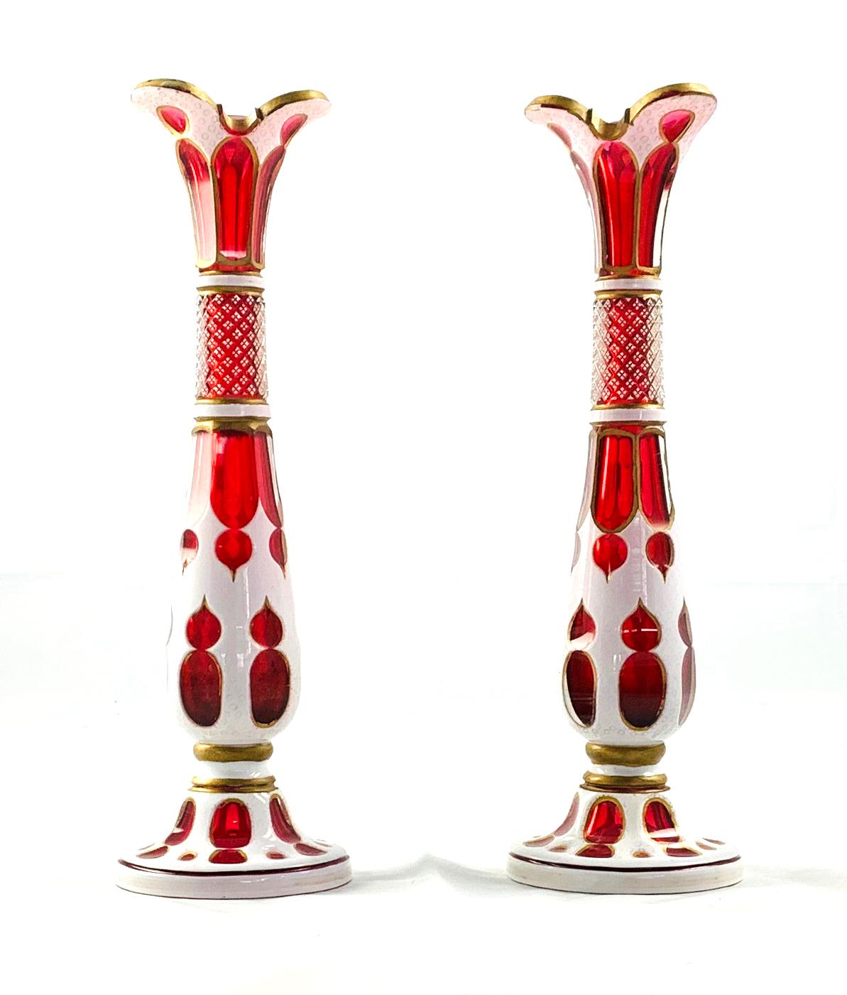 A fine pair of Bohemian Ruby glass vases with white enamel decoration, circa 1890. Each of long slender baluster form with gilt decorated wavy rim. Circular base.