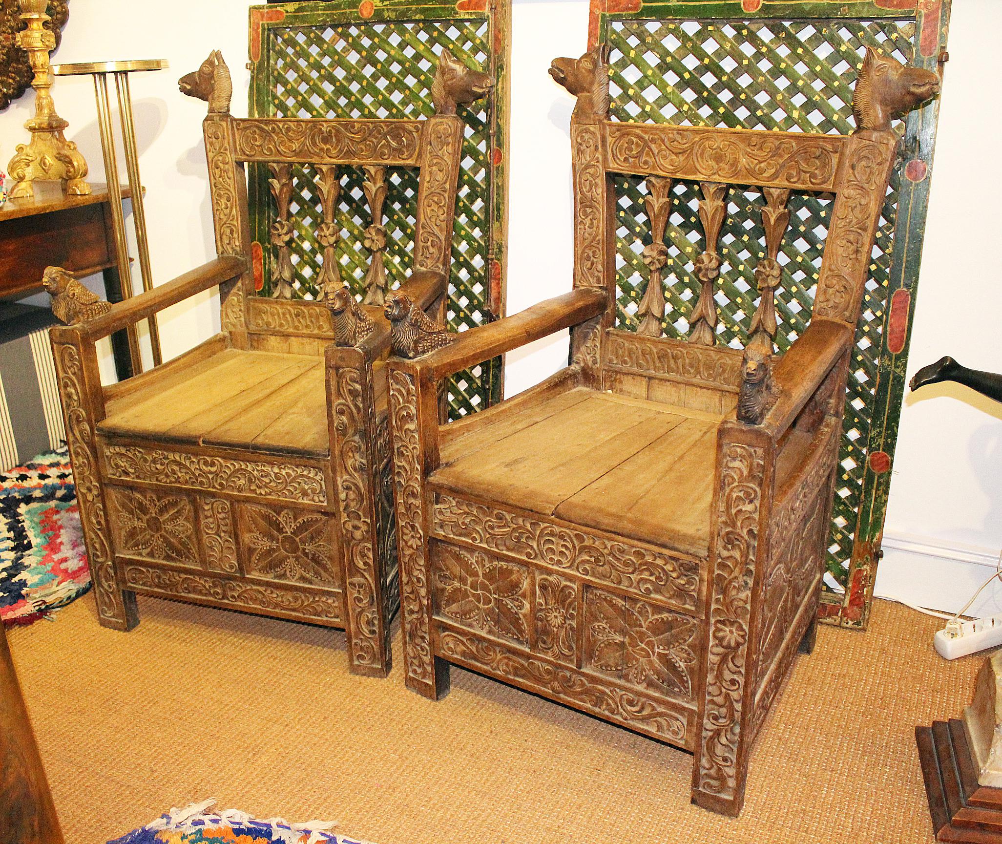 paire de fauteuils boliviens en bois sculpté à la main, datant du 19e siècle, décorés de motifs géométriques et d'animaux sur les bras et le dossier.