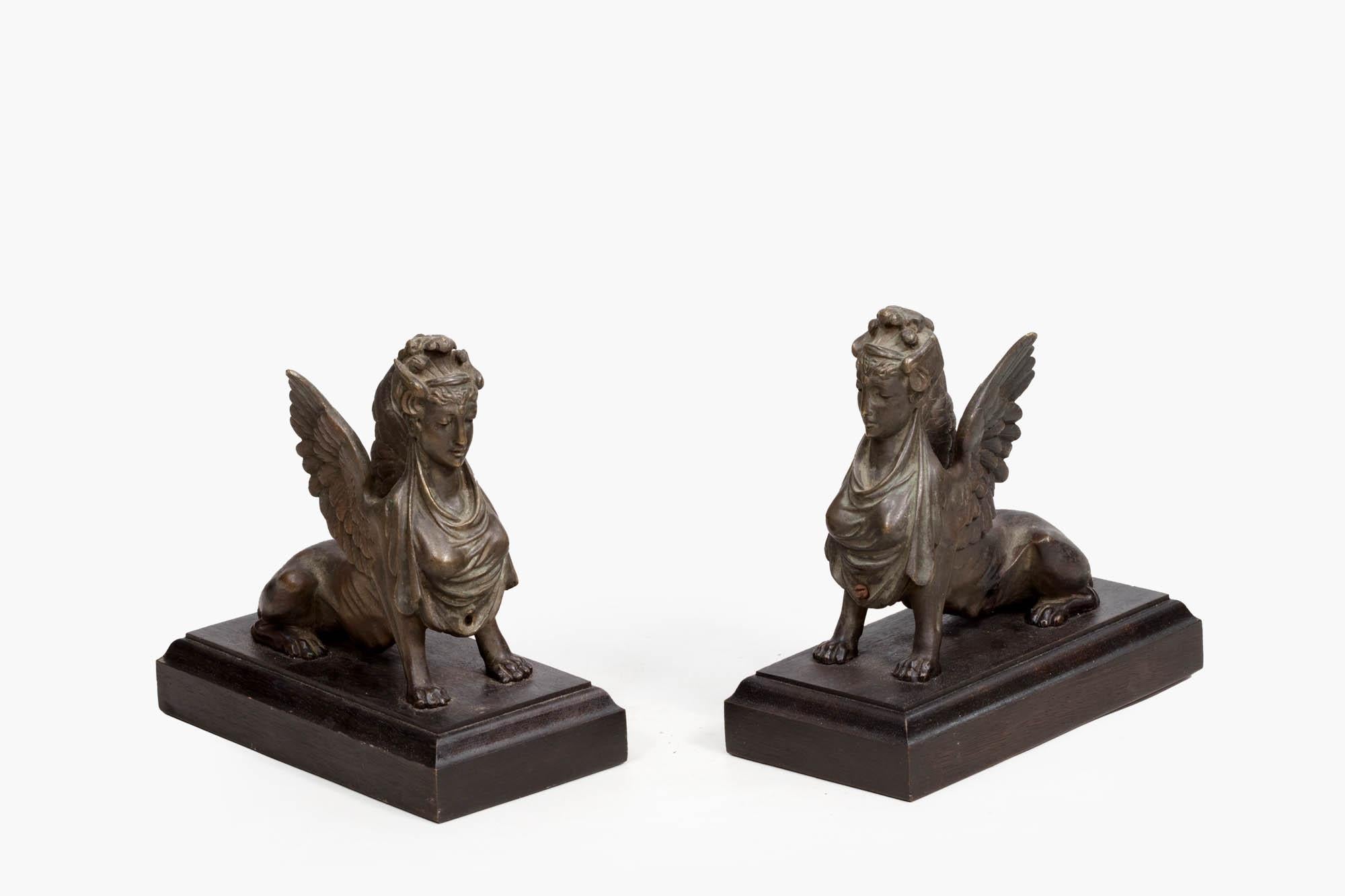 19th century pair of bronze Egyptian Revival sphinx figures in reclining poses seated on solid wooden rectangular plinth bases. A well-detailed pair with extended eagle wings drawn back over lion bodies, elegant headdresses and draped robes.