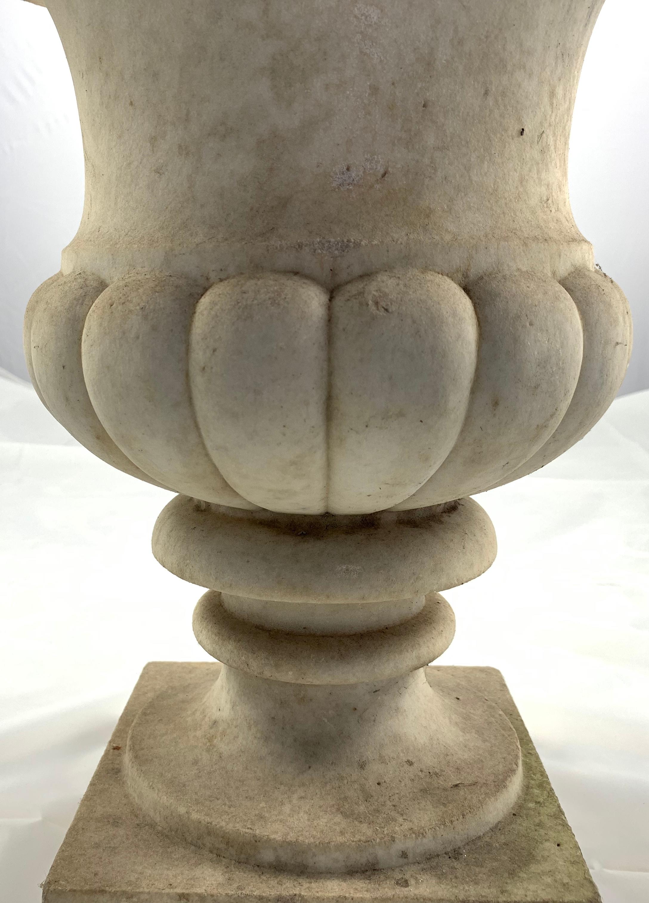 A pair of Carara marble Campana shaped garden urns, 19th century. Each decorated with a continuous band of lobes. On short banded stem and square base.