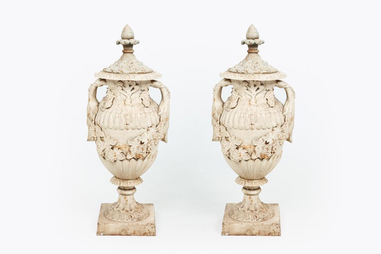 Pair of 19th century cast iron decorative urns with lids. Of unusual size and heavily decorated with classical motif, including anthemion and acanthus. Generously swagged with bunches of grapes.
 