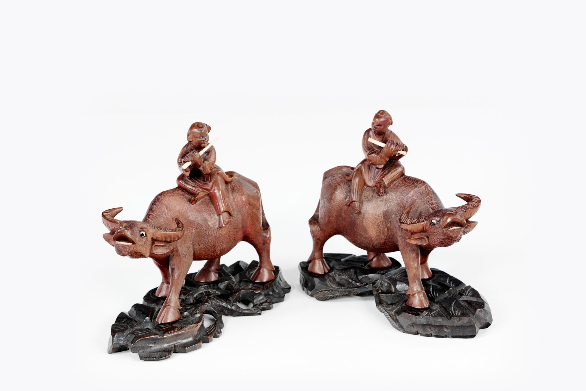 19th Century pair of dark hardwood water buffalo with inset glass eyes. These finely carved and highly detailed figures have carved boy figures sitting on their backs holding bone flutes. Both sculptures sit atop separate carved hardwood stands.