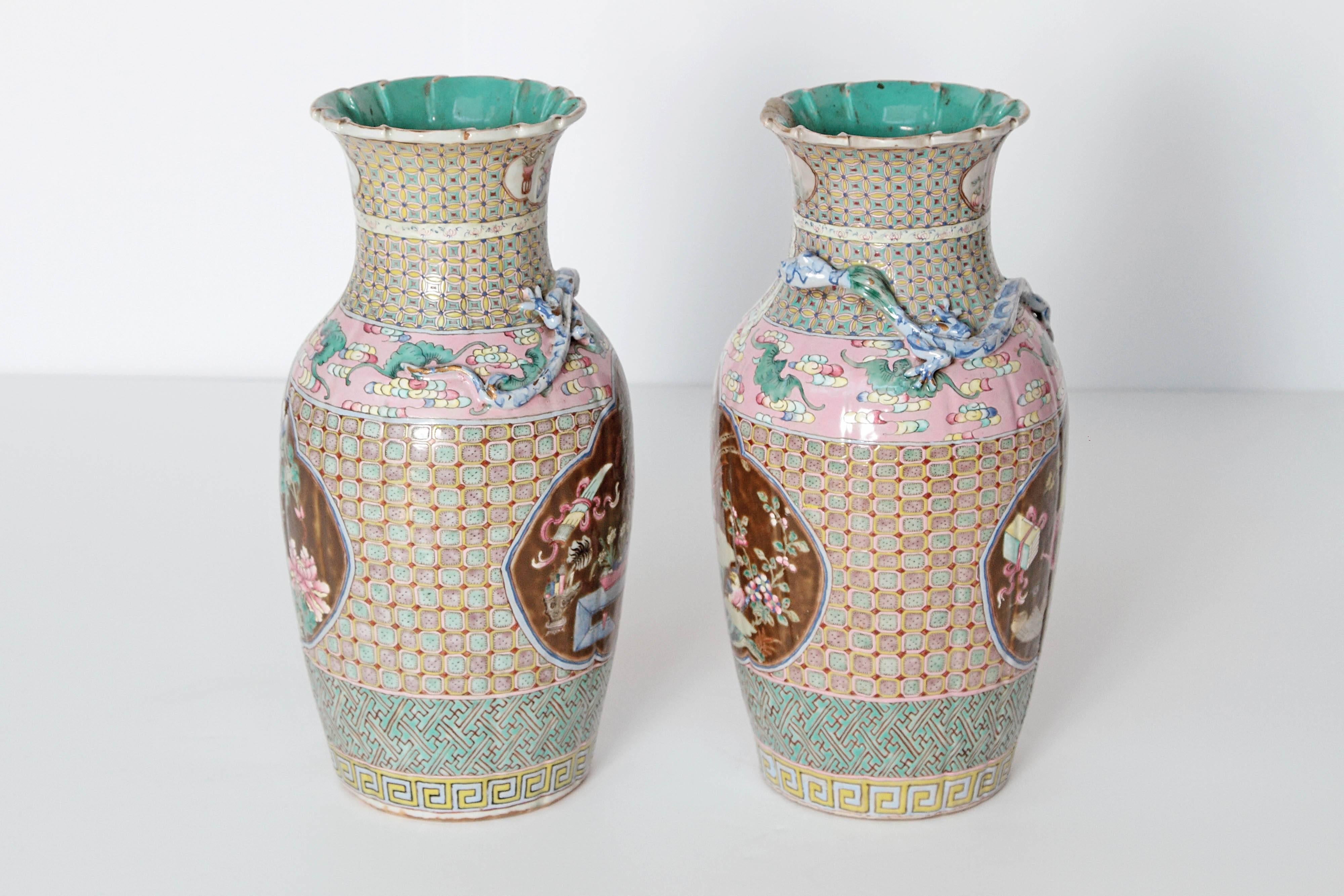 A pair of Chinese vases with all over variety of patterns on pink and turquoise with cartouches of brown background with floral and fauna on one side and dragon and treasures on the opposite side. Applied dragon on neck. Ruffled rim. Drilled for